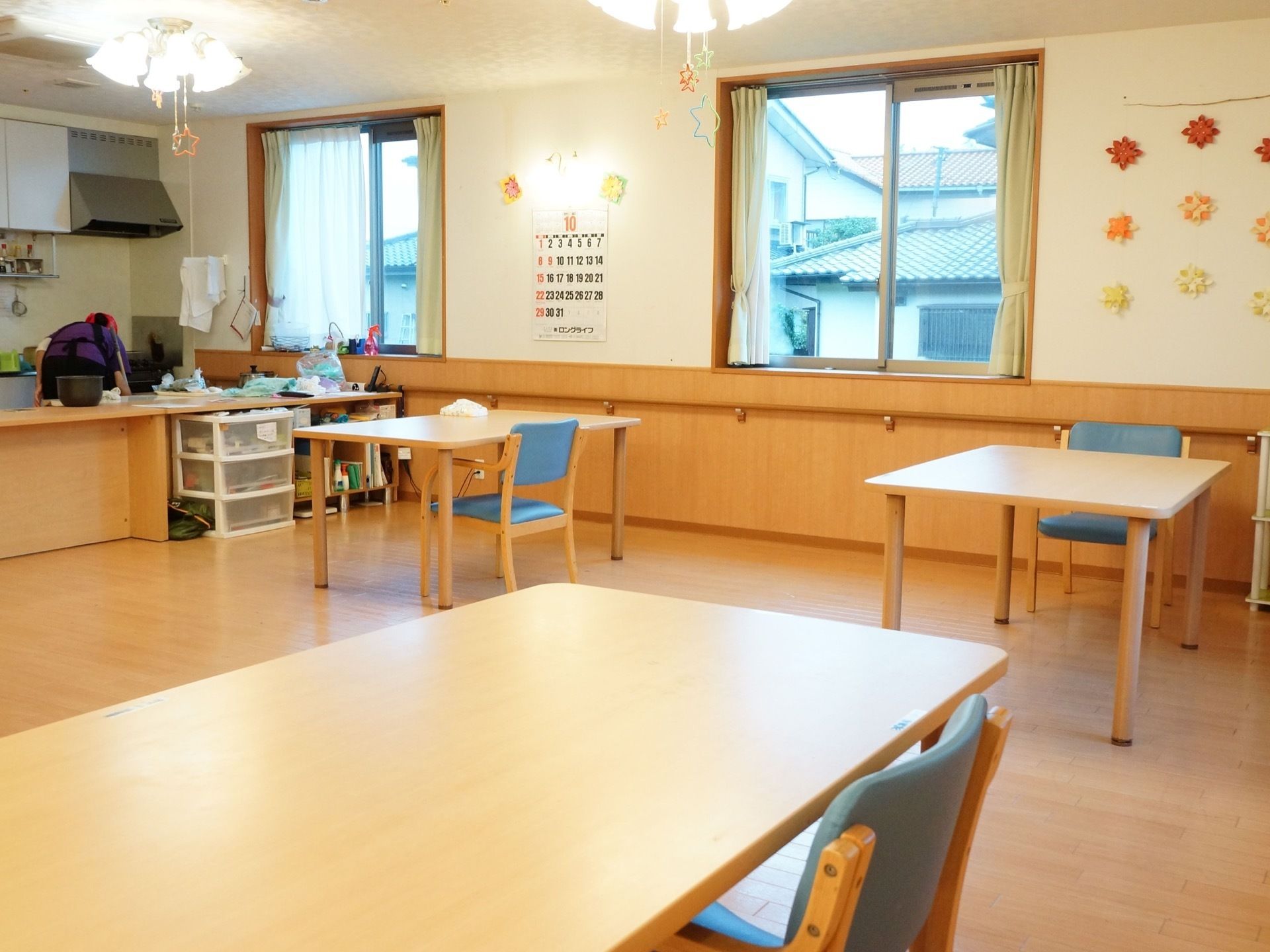 広々としたダイニングルームには、イスやテーブルが置かれている。また壁には窓があり、カレンダーがかけられている。