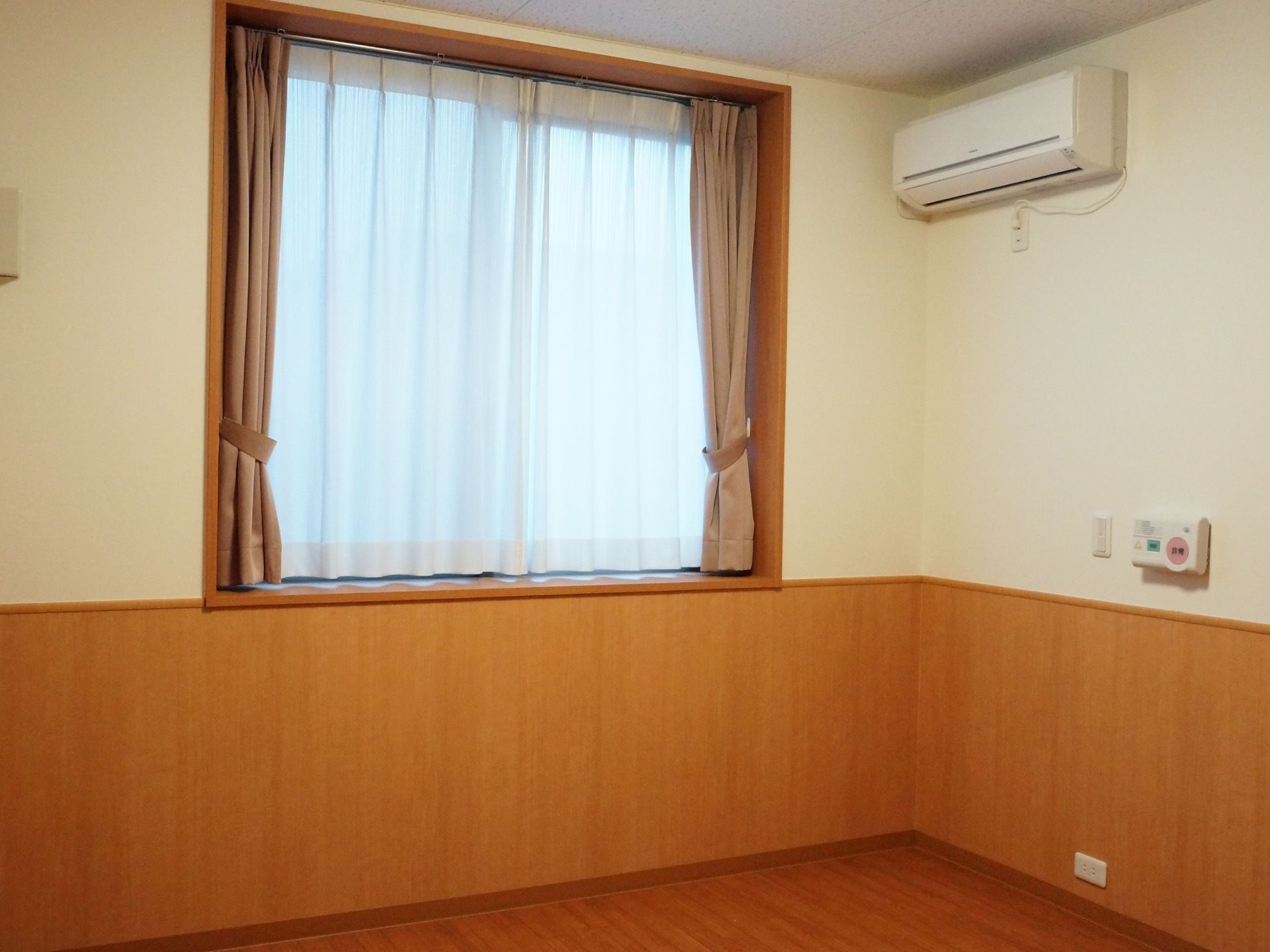居室にはガラス窓があり、遮光カーテンとレースカーテンを備え付けている。また壁には空調設備を設置している。