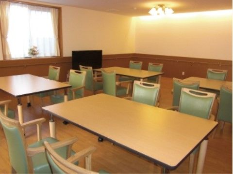 高さが調節できるテーブルと肘掛椅子が並んだ、テレビのある食堂