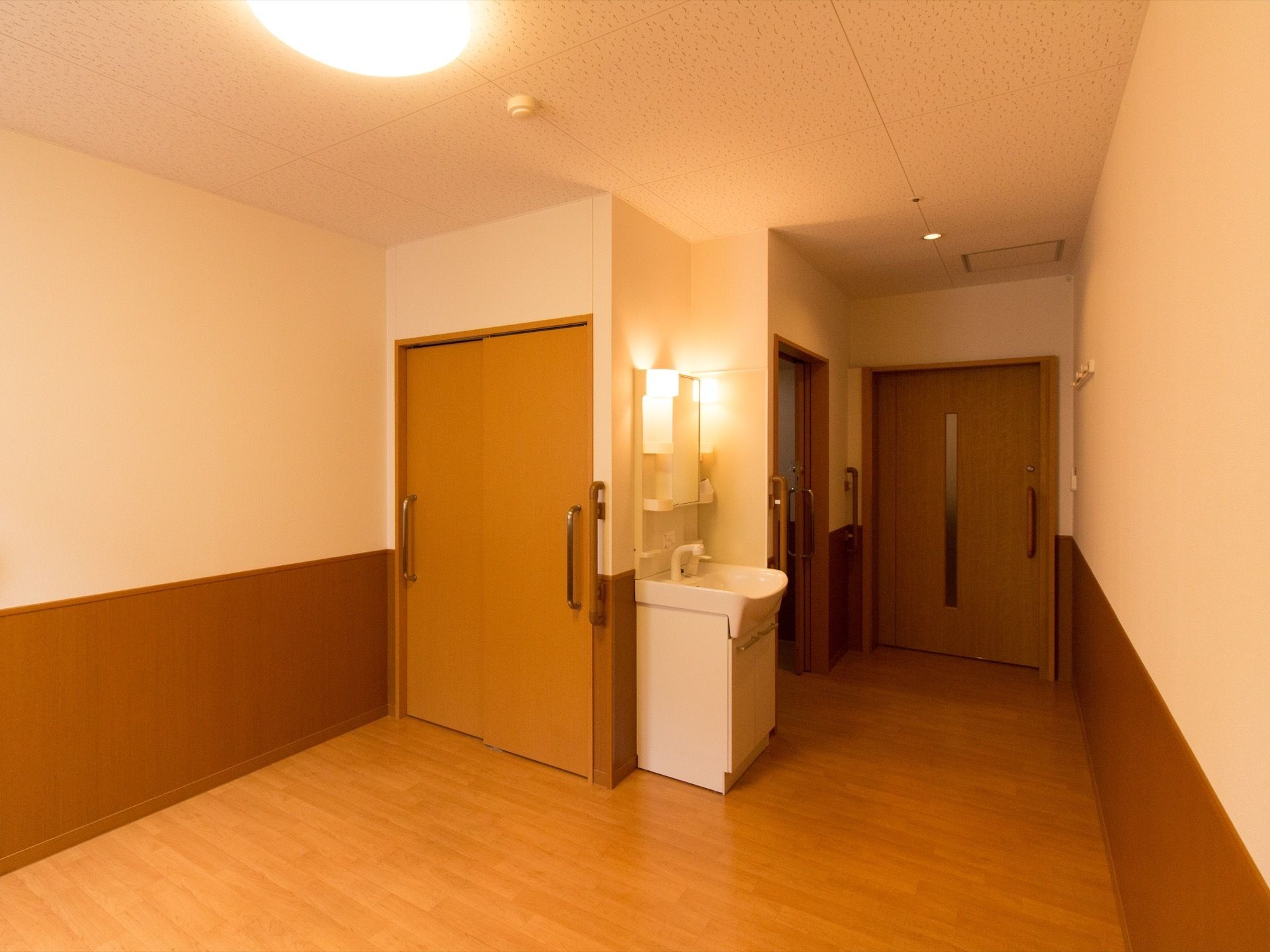 部屋の照明は暖かな印象の電球色になっている。入って右側にトイレスペースがあり、すぐ傍に洗面台が設置されている。