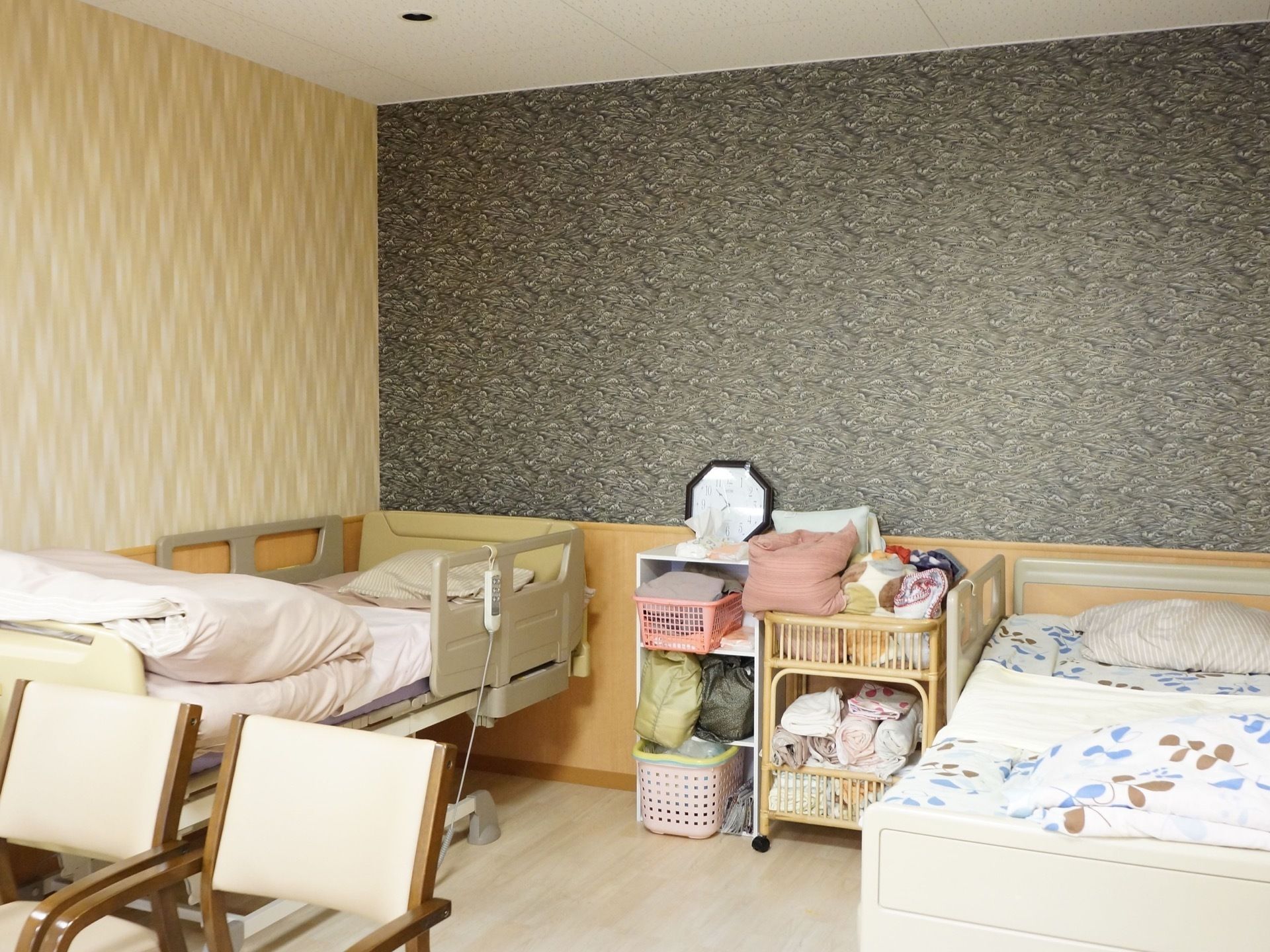 電動ベッドを２台設置した居室。手前には椅子が２脚設置されている。ベッドの間には、時計をはじめ生活雑貨が置かれている。