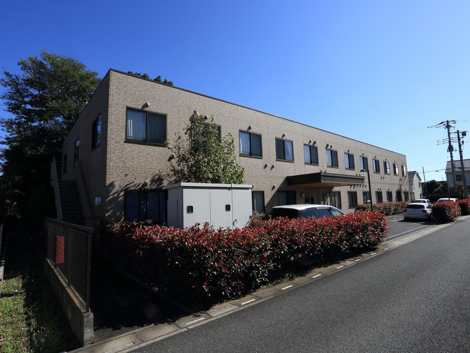 ２階建ての幅の広い施設の外観。２階の端の部分に外階段が設けられている。車道からは施設の建物が見付けやすくなっている。