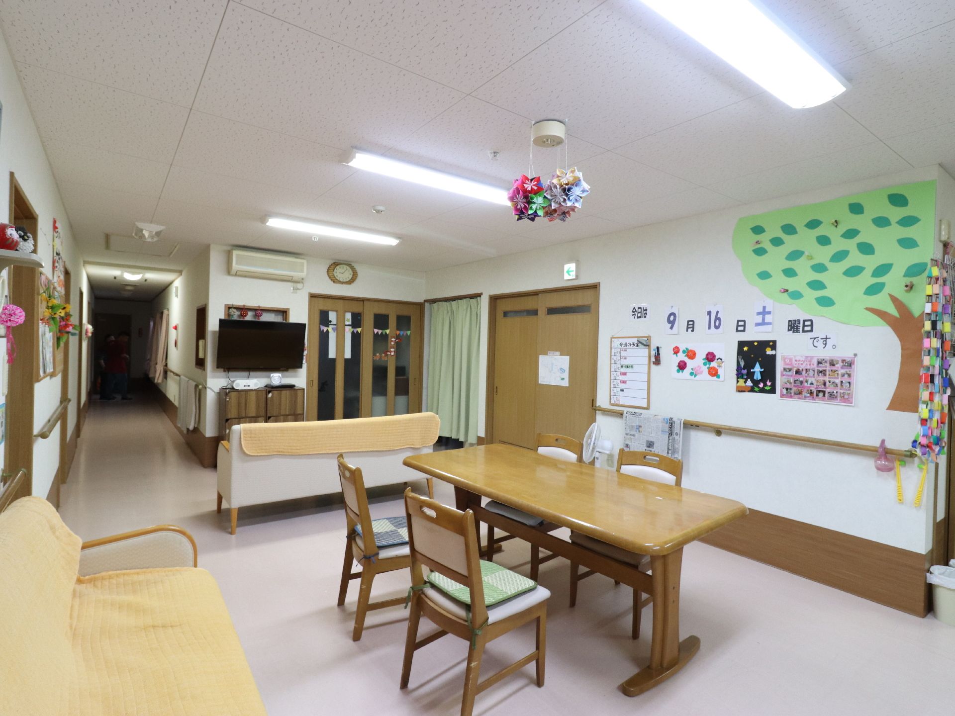 入居者様が自由に出入りできるように、廊下との仕切りをなくしている。またテーブルは車イスの人のために、ゆとりをもたせた配置となっている。