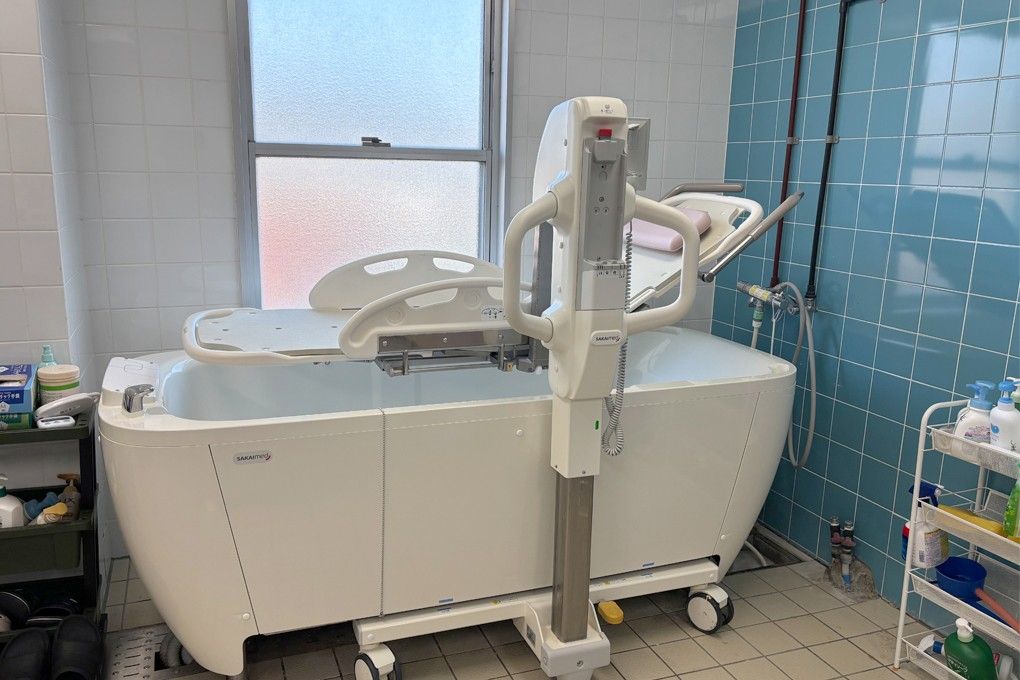 白色と青のタイルで囲まれた浴室である。左側には窓が１ヵ所ある。中央には座った状態で入浴できる介護浴槽が設置されている。