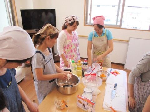 エプロンと三角巾をつけた数人の女性が、料理をしている様子