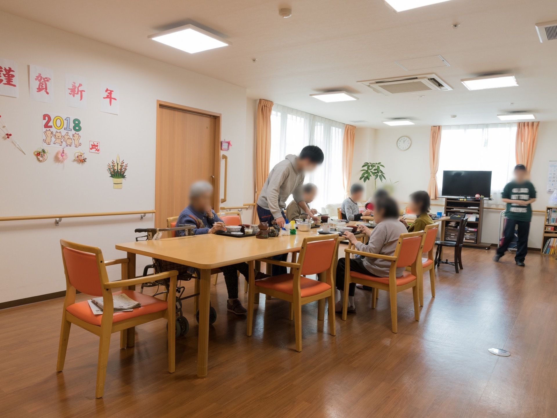日当たりがよく、広々とした共有スペースである。長テーブルが設置されている。テレビや本棚が設置されている。