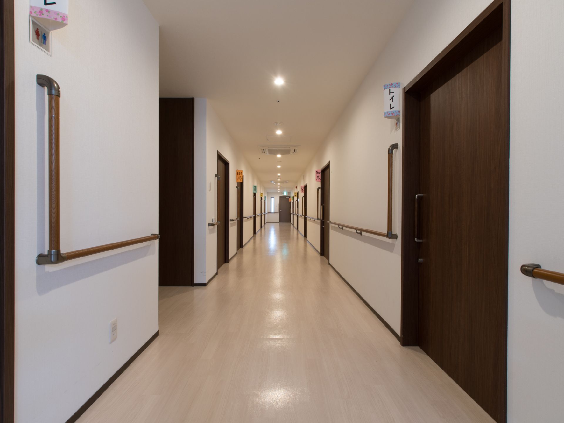 白い壁と木目のドアで明るく清潔感のある廊下。共同トイレは入居者の個室近くにあるので夜中でも行きやすい。