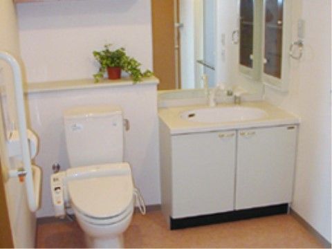 フローリング床に白い壁紙の清潔な温水洗浄便座付きのトイレ。トイレの横には、大きな鏡のついた手洗いシンクがある。