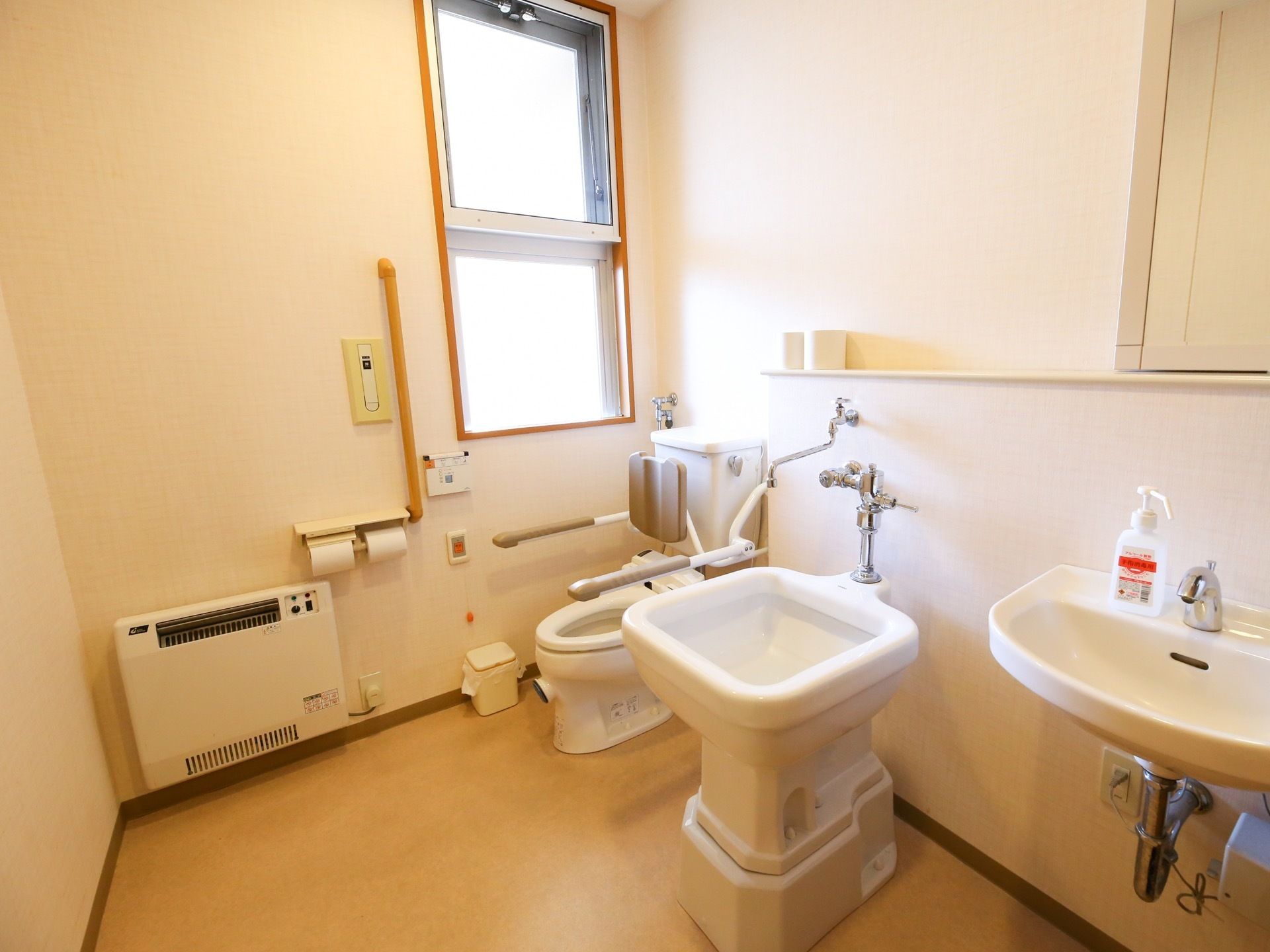 窓のあるトイレに、洋式便座とオストメイト対応トイレがある。温水洗浄式の便座の操作ボタンは壁に付いている。