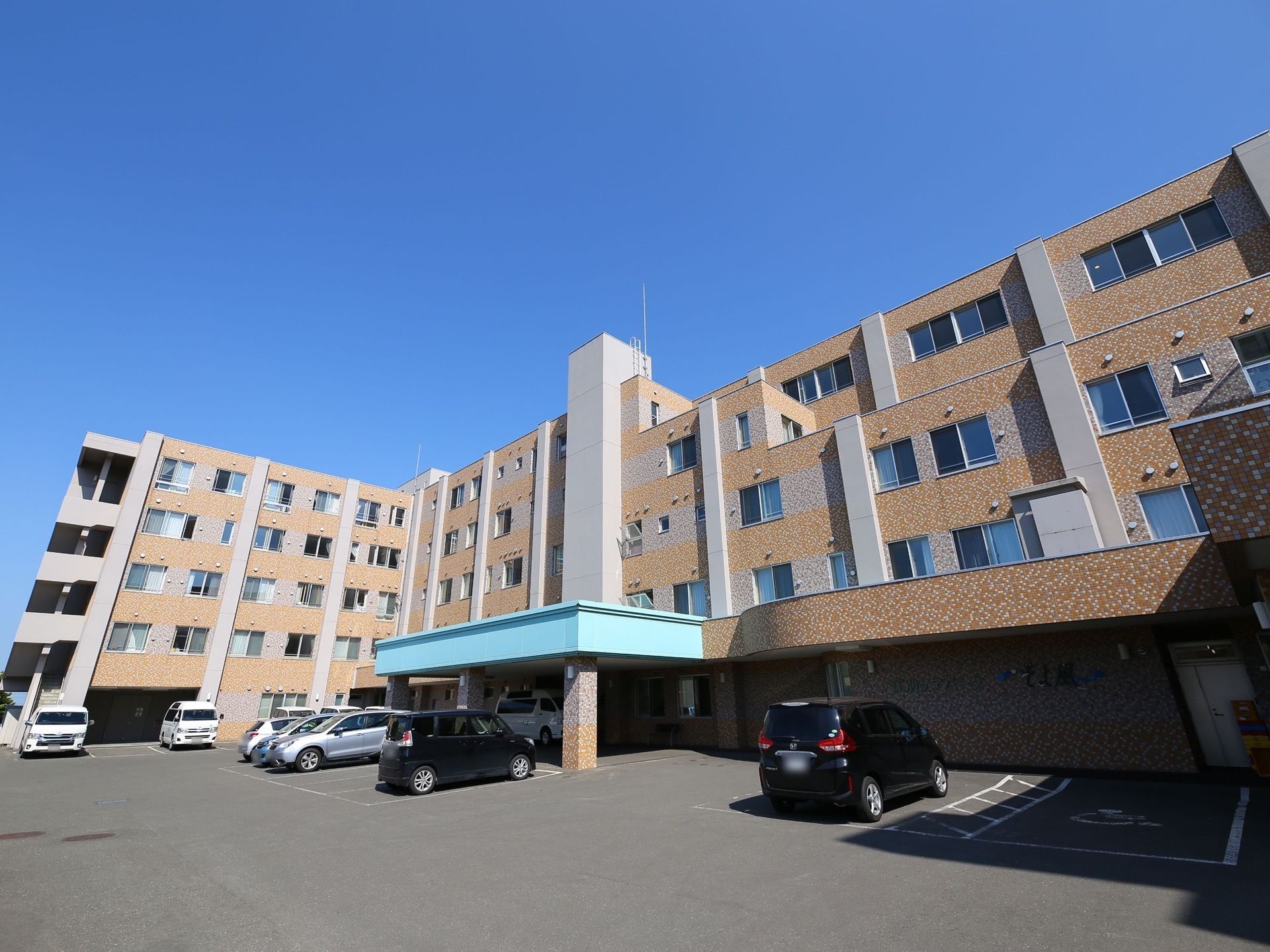 レンガ積み模様の壁と白色の柱の外観を持つ５階建ての施設である。玄関前に大きな車寄せがあり、車が停まっている。