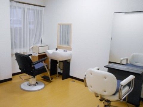 白と黒を基調にしたシックな内装に、リクライニングチェアと洗髪器が設置されている。隣には鏡台とひじ掛け付きの椅子が置かれている。