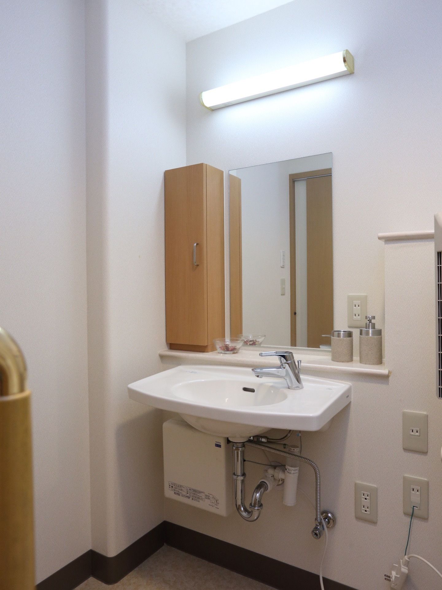 トイレ内に設置されている洗面台には、大きな洗面ボウル、鏡、棚、照明、コンセントの差込口が備わっている。