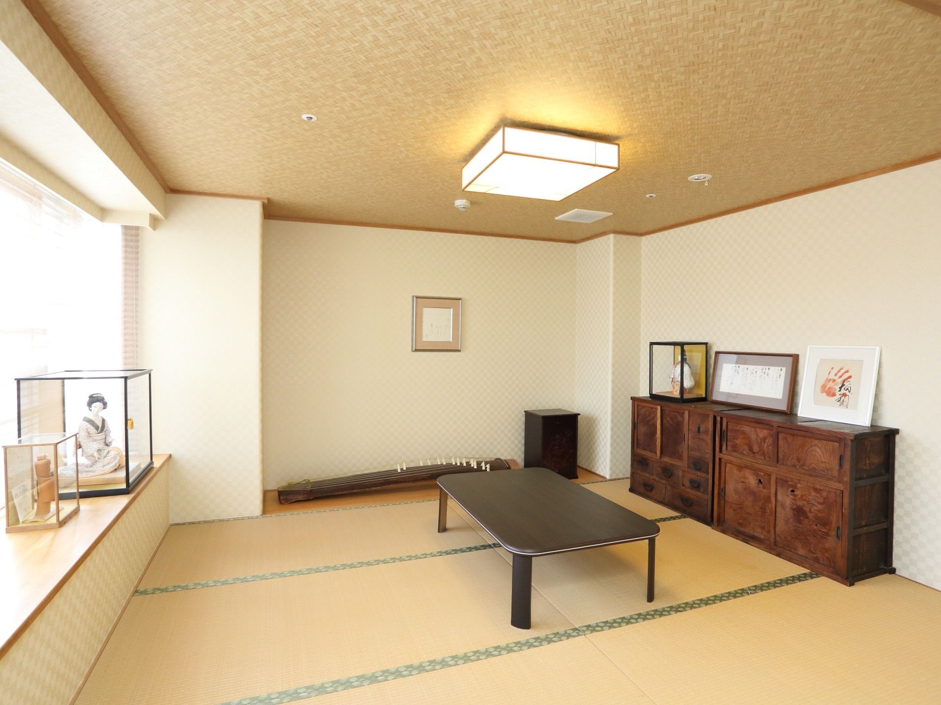 採光に配慮された明るい和室コーナー。部屋の中央にはテーブルが配置されている。和箪笥に日本人形、琴などが備わっている。