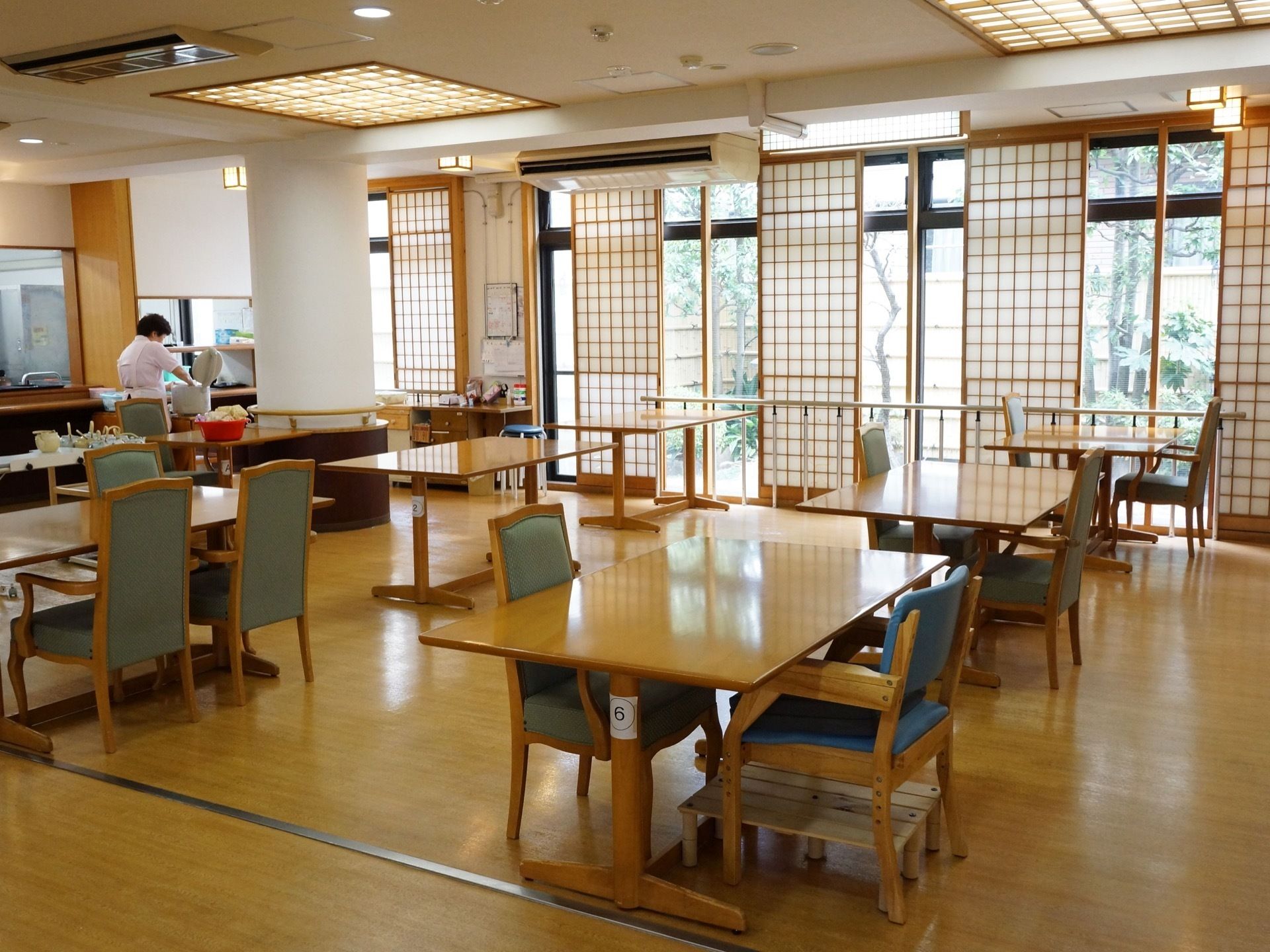 食堂には大型の窓があり、障子が取り付けられている。窓の向こうには、たくさんの草木が見える。左端には丸い大きな柱がある。