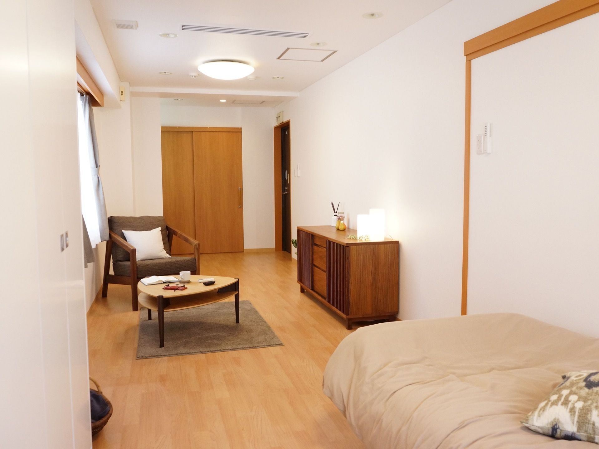 居室の出入口は、木目調デザインの大きな引き戸になっている。左端にソファーチェアがあり、四角いクッションが置いてある。