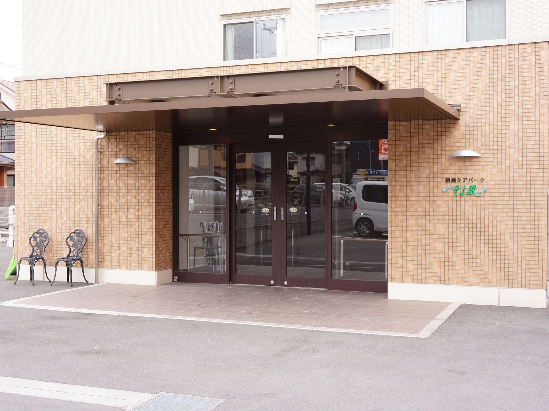 両開きタイプの自動ドアが設置されている施設の入り口。アプローチは段差がなく、入り口の横には椅子が置かれている。