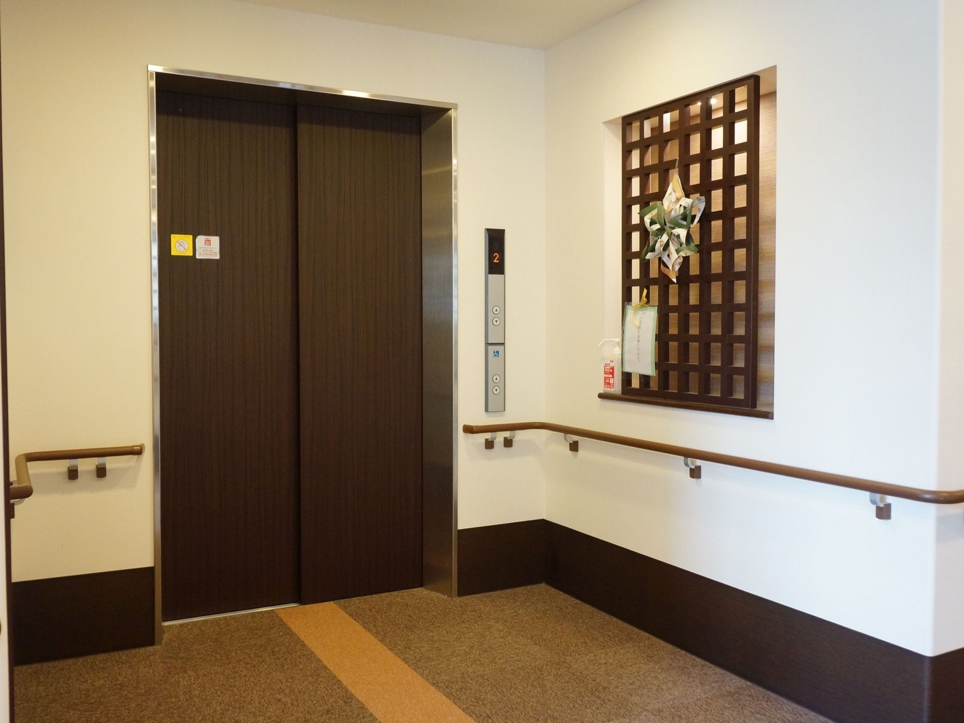 間口が広いエレベーターが設置されている。扉周辺には手すりが設置されている。壁にはペーパークラフトが飾られている。