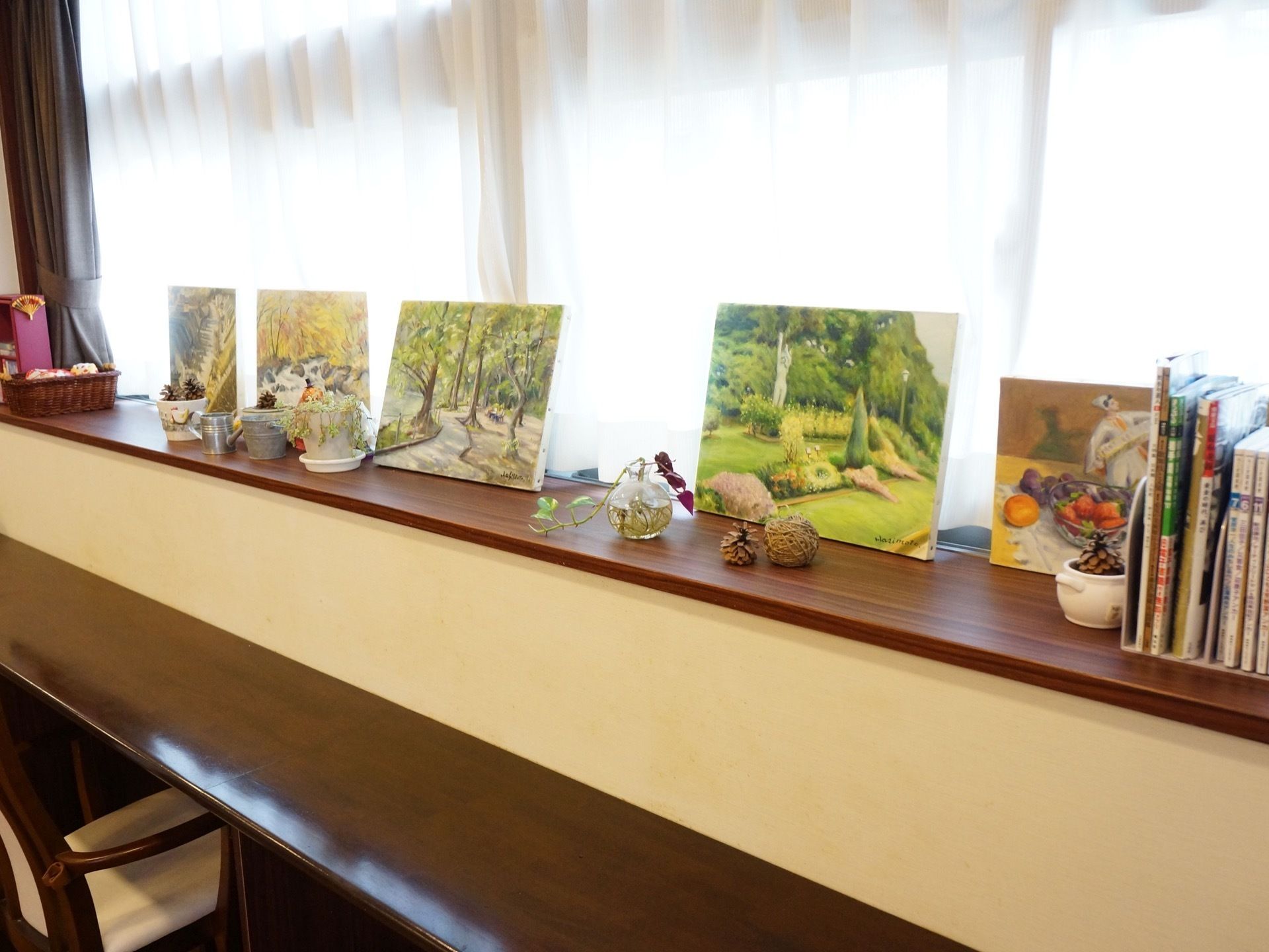 共有スペースの窓際には、5枚の絵画や本、植物などが飾られている。そばには、カウンターと椅子が設置されている。