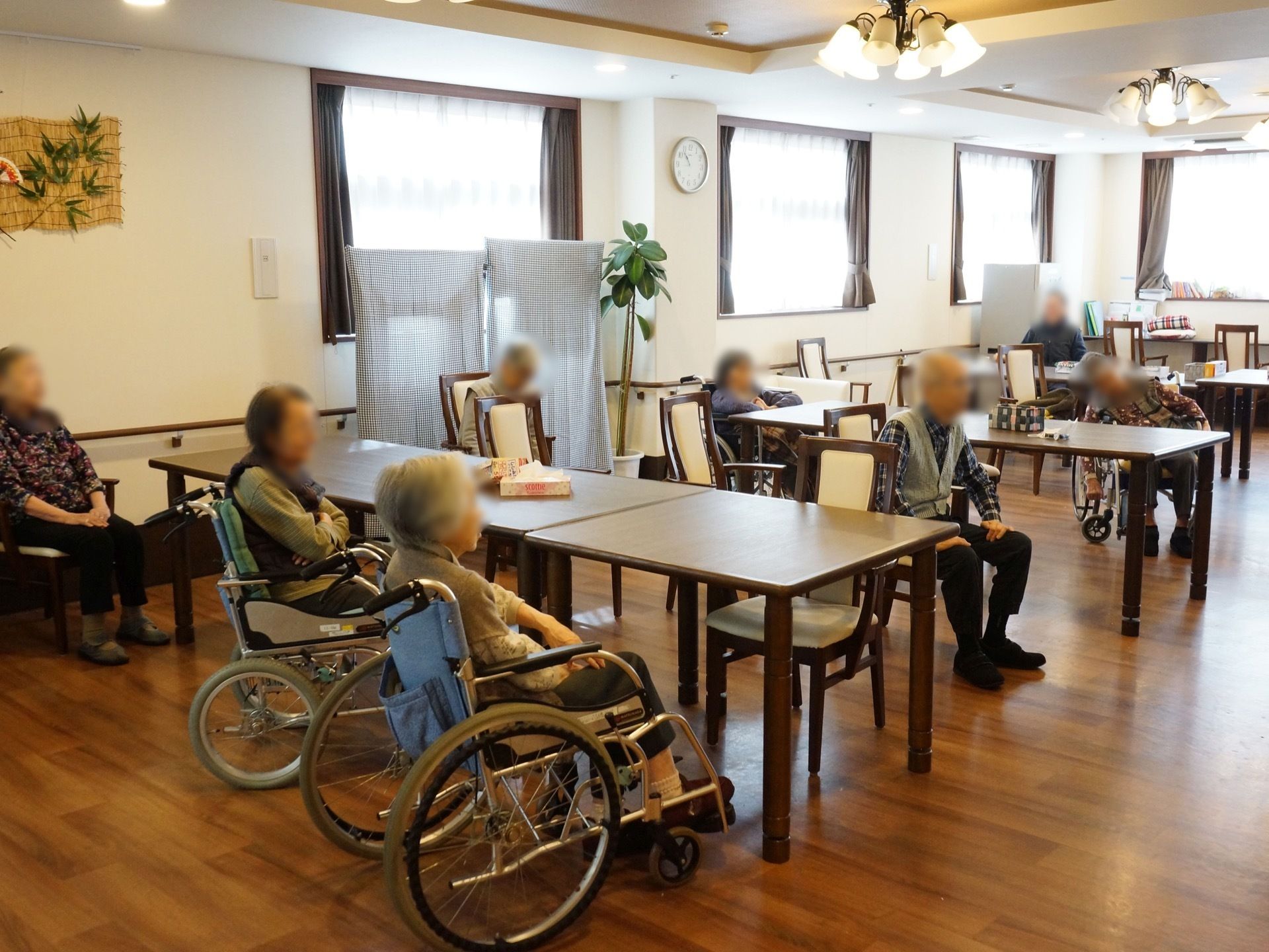 広い食堂にダイニングテーブルが並べられている。壁に沿って手すりが設置されており、観葉植物が壁際に置かれている。