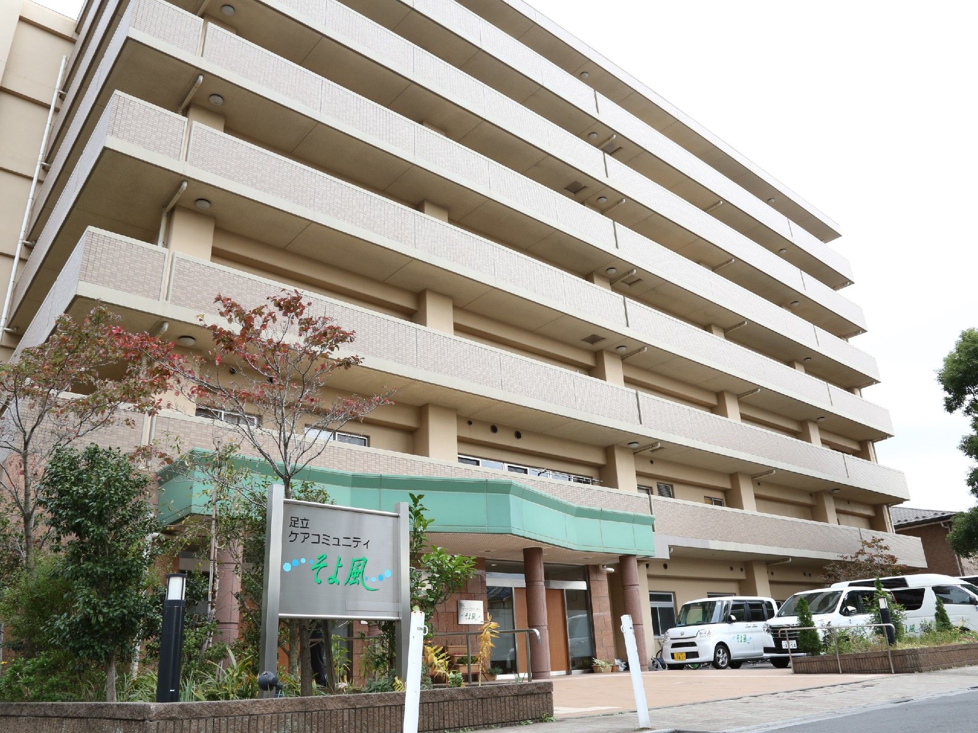 マンションのような外観の施設は、敷地内に駐車場を設けている。入り口付近は当施設の看板を設置している。