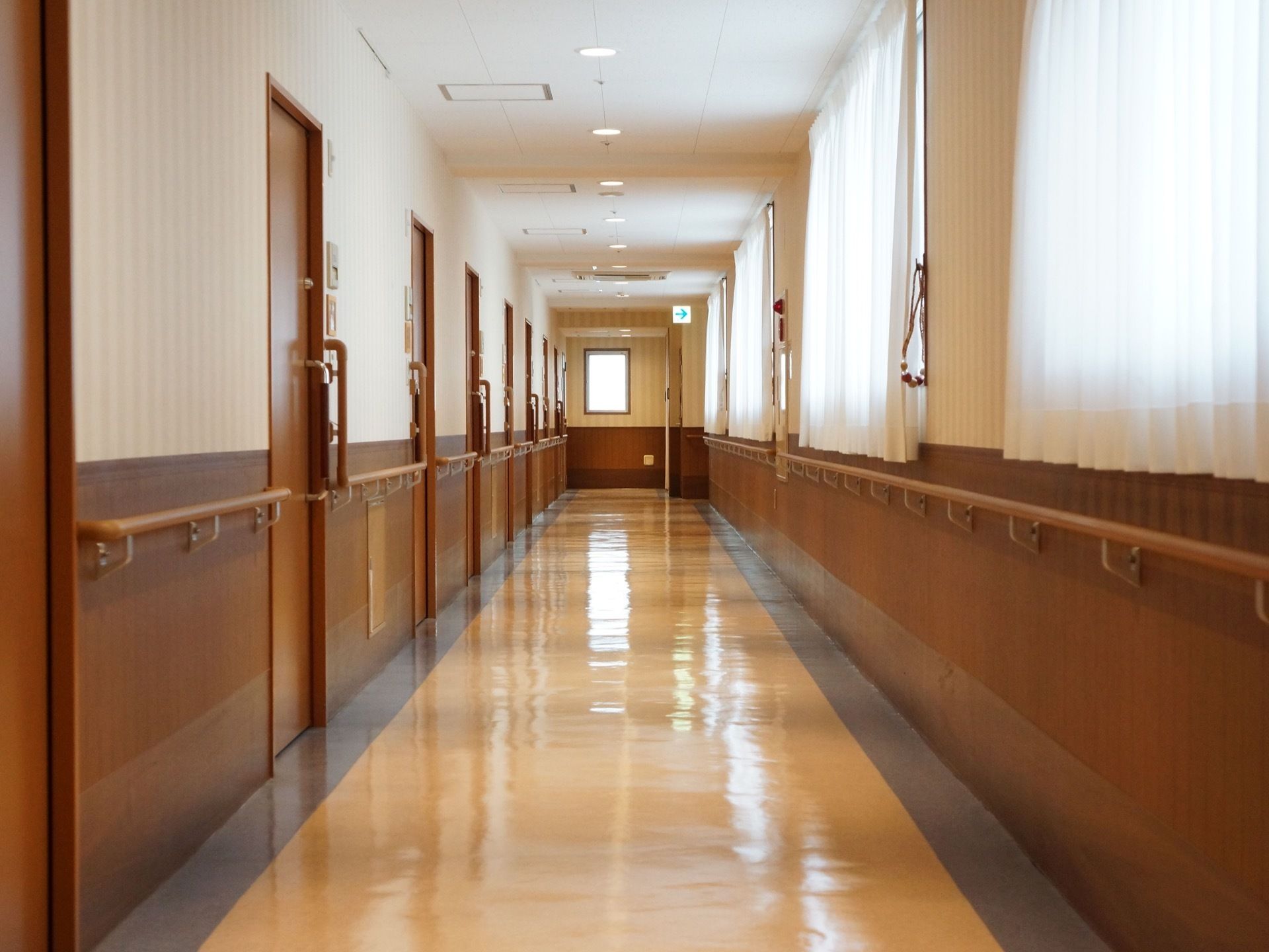 奥行きのある明るい共用廊下である。全面の壁の腰高あたりには、転倒防止のための木製手すりが設置されている。