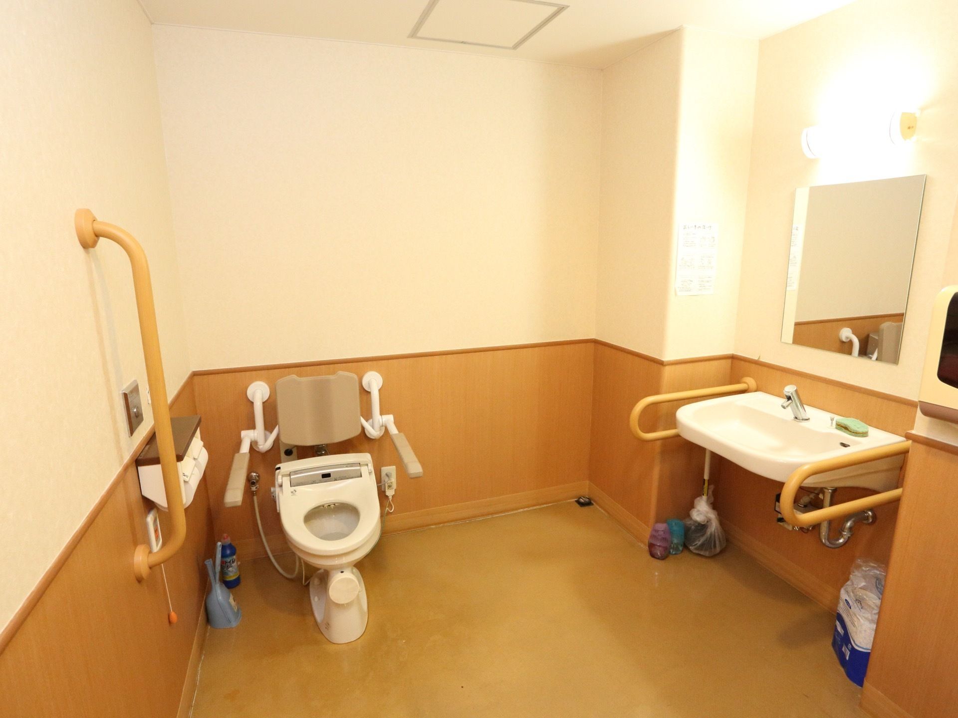 共用トイレは広々としたスペースとなっている。便座、洗面台に手すりが設置されている。便座はひじ掛け、背もたれ付きである。