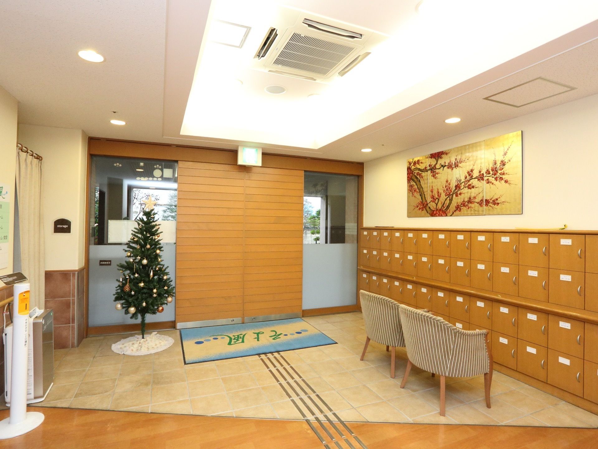玄関には扉付きの下駄箱が置かれている。椅子が置いてあり座れる。施設名の入った玄関マットが敷かれている。