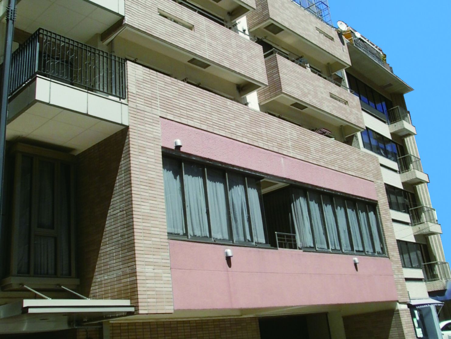 高級感のあるタイル張りの外壁の、マンションのような大規模な建物である。カーテンの掛かった大きな窓がある。