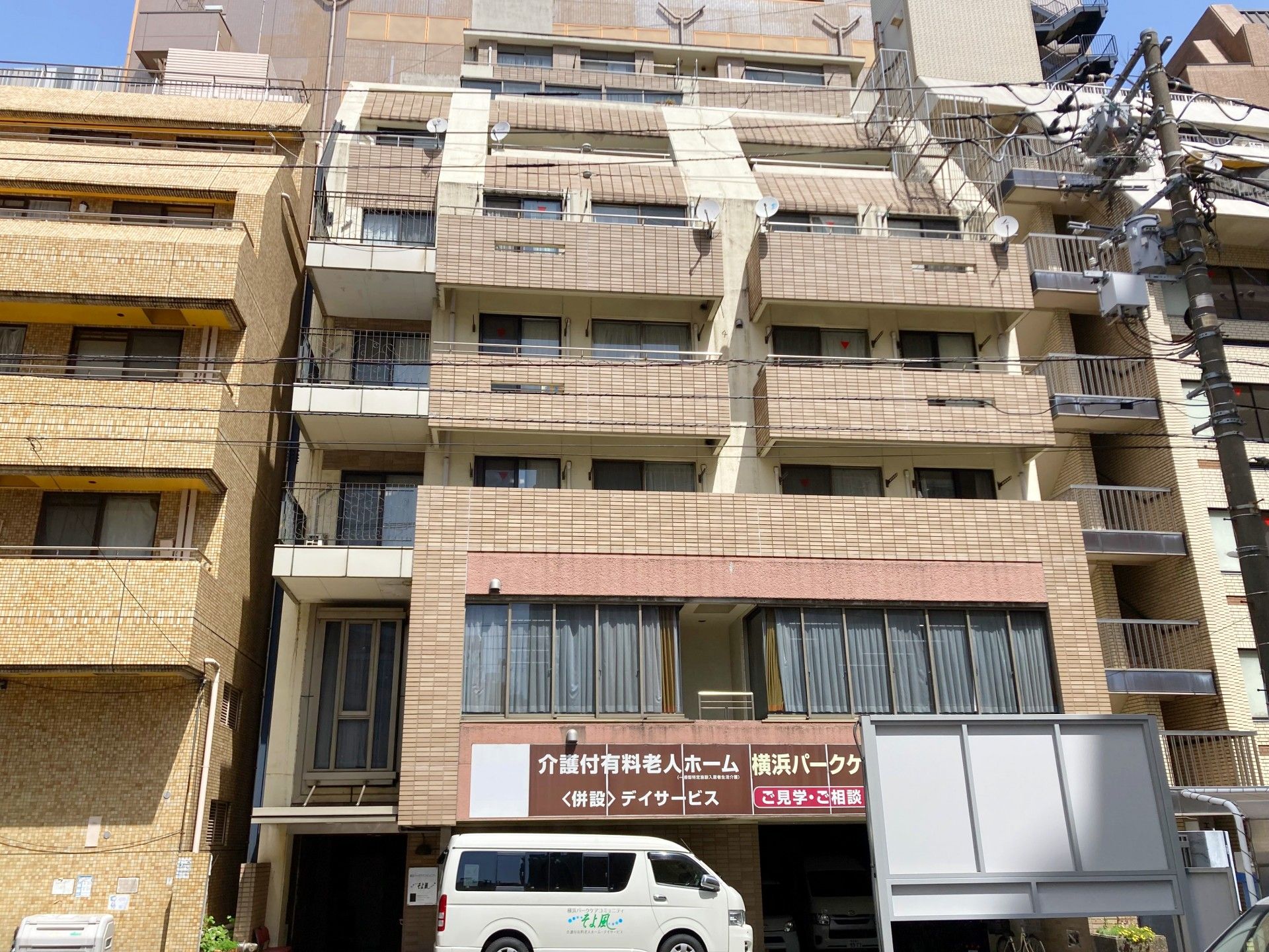 一般的な集合住宅と変わらない、タイル張りの外観。１階部分に駐車場がある。エントランスは段差がなく、車椅子をご利用の方も安全に通行できる。