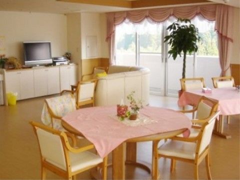 ピンクのクロスがかけられたテーブルの上に、可愛らしいアレンジの花が飾られている。壁際のテレビの前にはソファが置かれたコーナーがある。