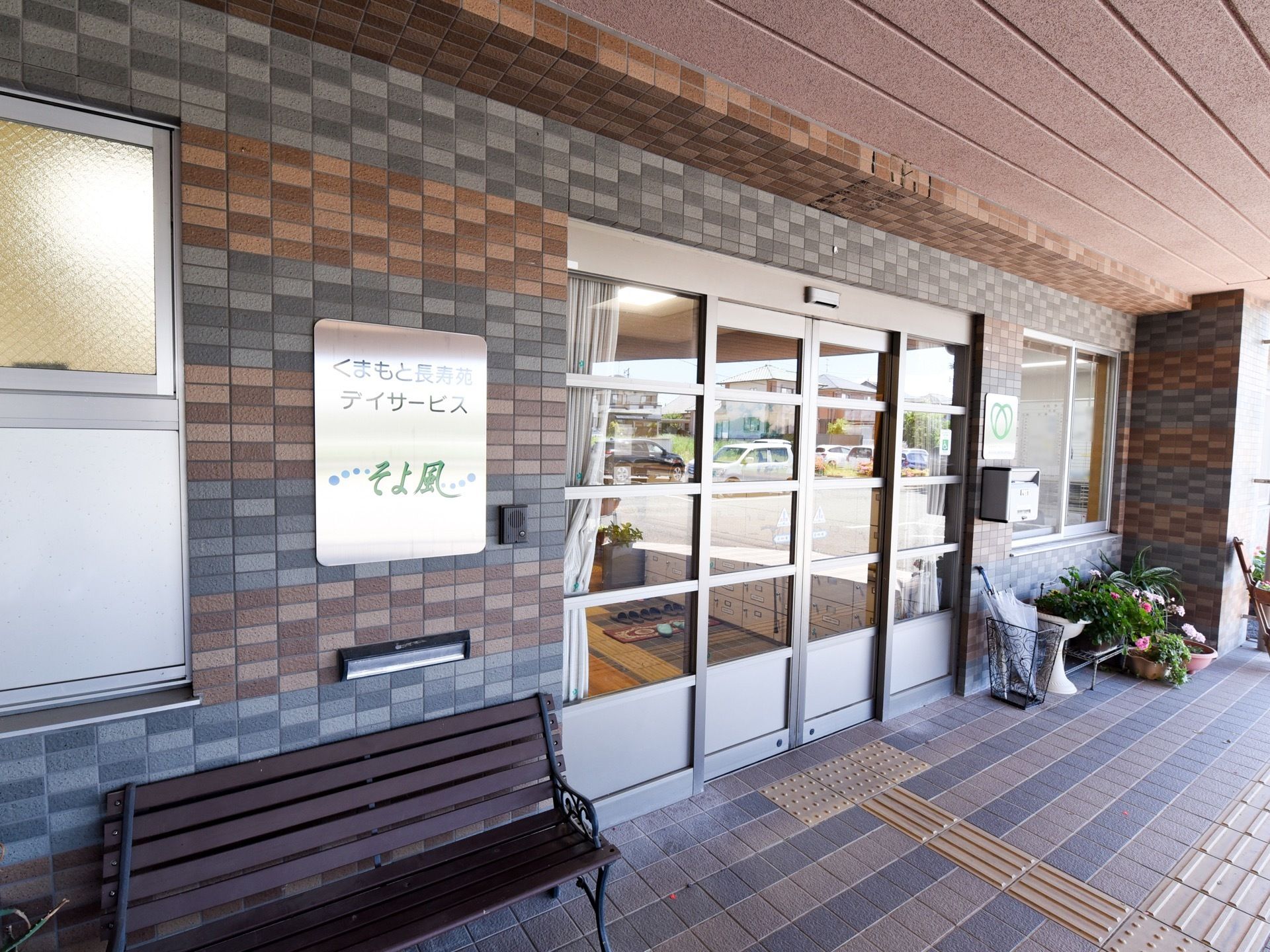 上部が屋根に覆われたレンガ調の入口である。自動ドアのすぐ手前まで点字ブロックが伸びており、壁には施設の名称が明るく表示されたタイルがある。