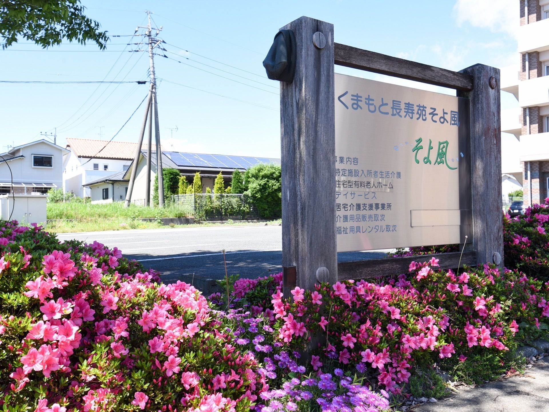 建物の側に木の枠で覆われた看板があり、施設の名称と提供している各種サービスが案内されている。看板の周りは豊かな草花で囲まれている。