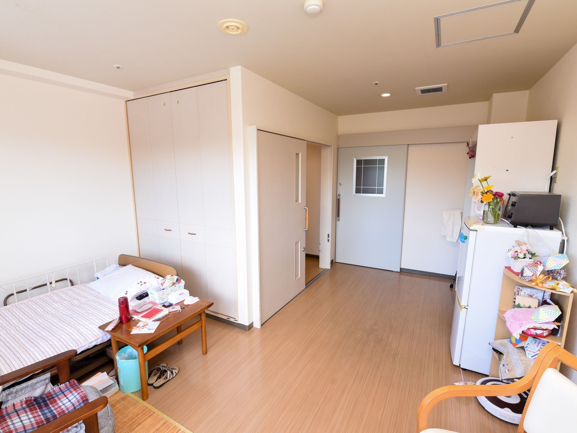 居室にはスライド式のドアを通じて出入りすることができ、優しい色合いのフローリングが敷かれている。室内中央には、広い空間が確保されている。