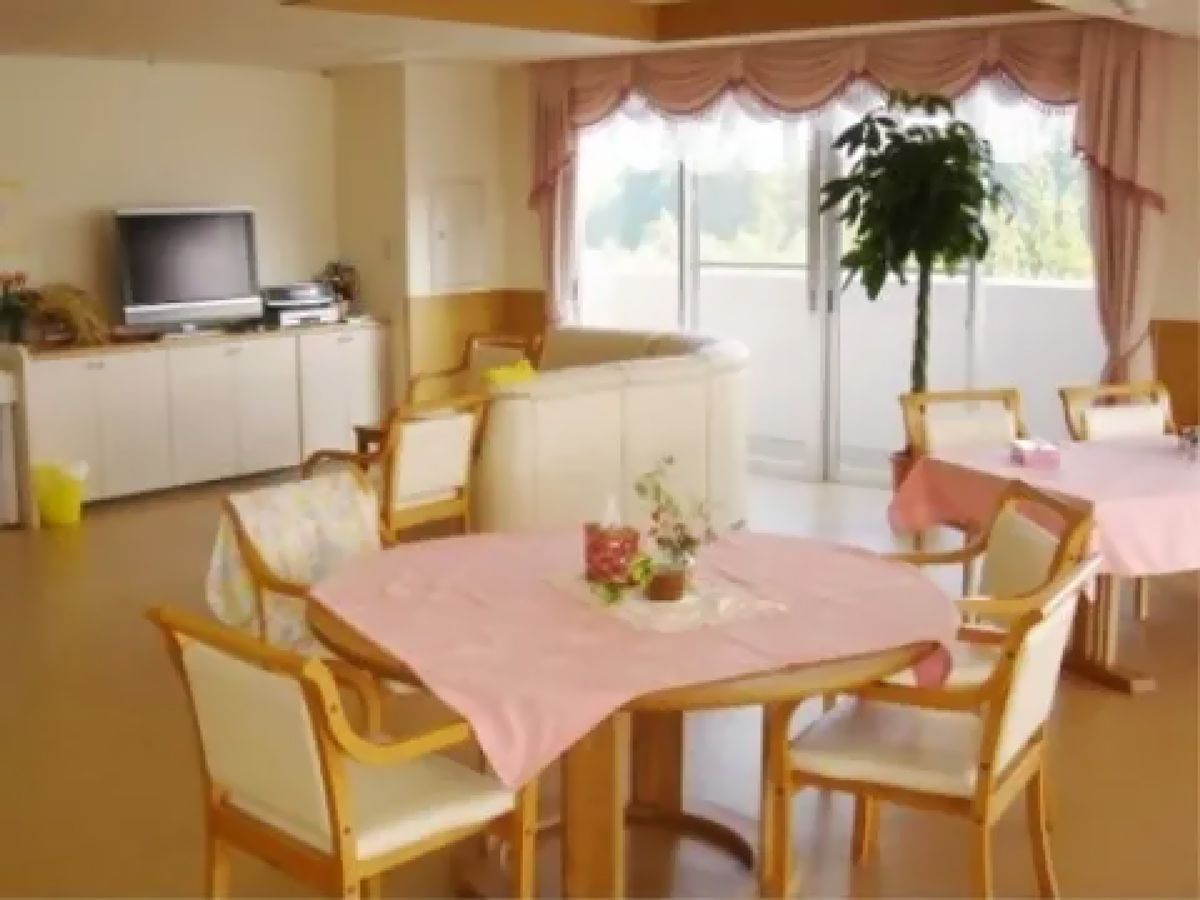 ピンクのクロスがかけられたテーブルの上に、可愛らしいアレンジの花が飾られている。壁際のテレビの前にはソファが置かれたコーナーがある。