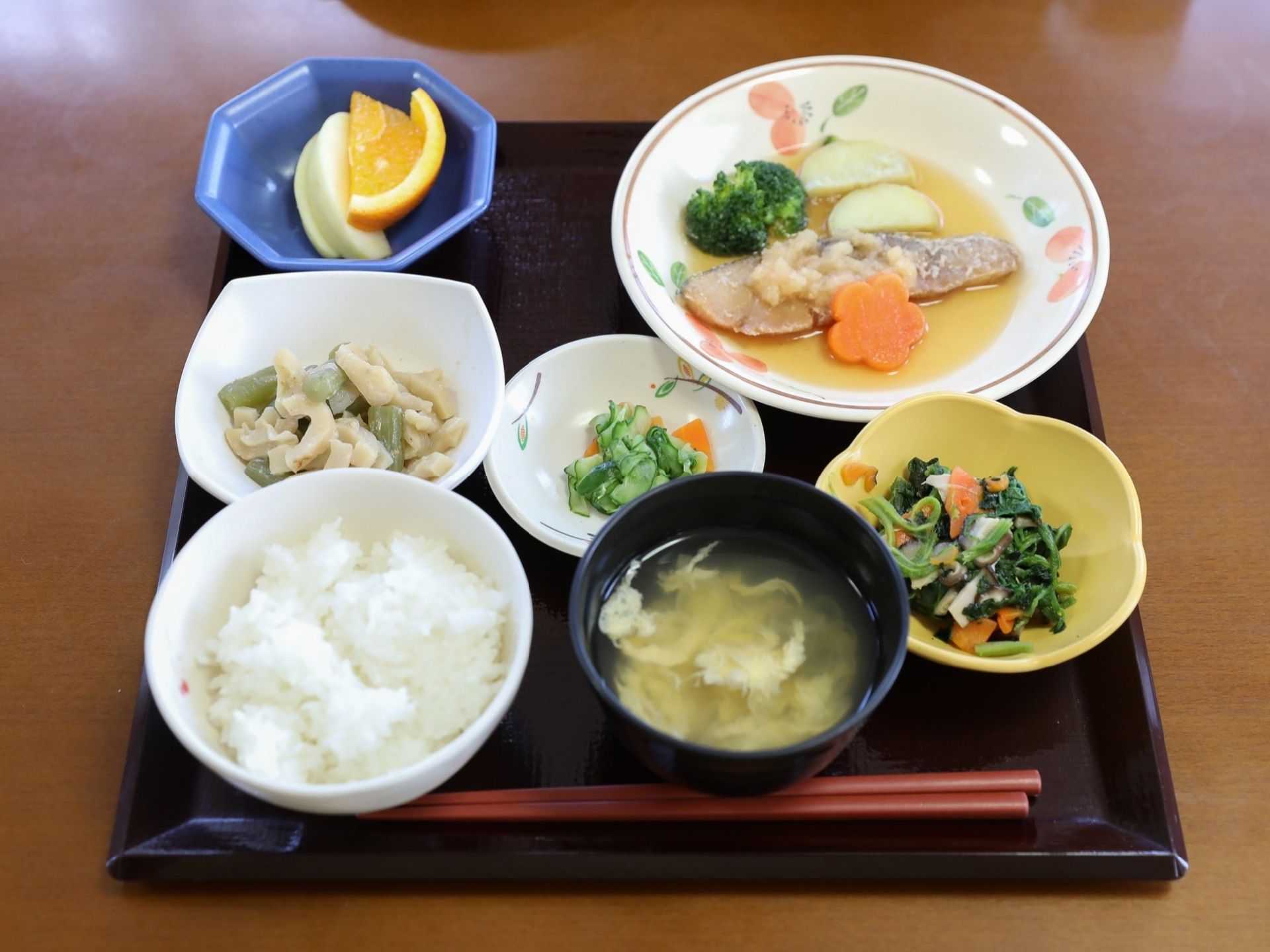 メイン料理は魚。主食、汁物に小鉢が３種類とフルーツが付いている。野菜を多く取り入れ、彩りもきれいに調理されている。