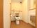 白い壁で清潔感のあるトイレになっている。便座とトイレットペーパーホルダーの近くには手すりが設置されている。