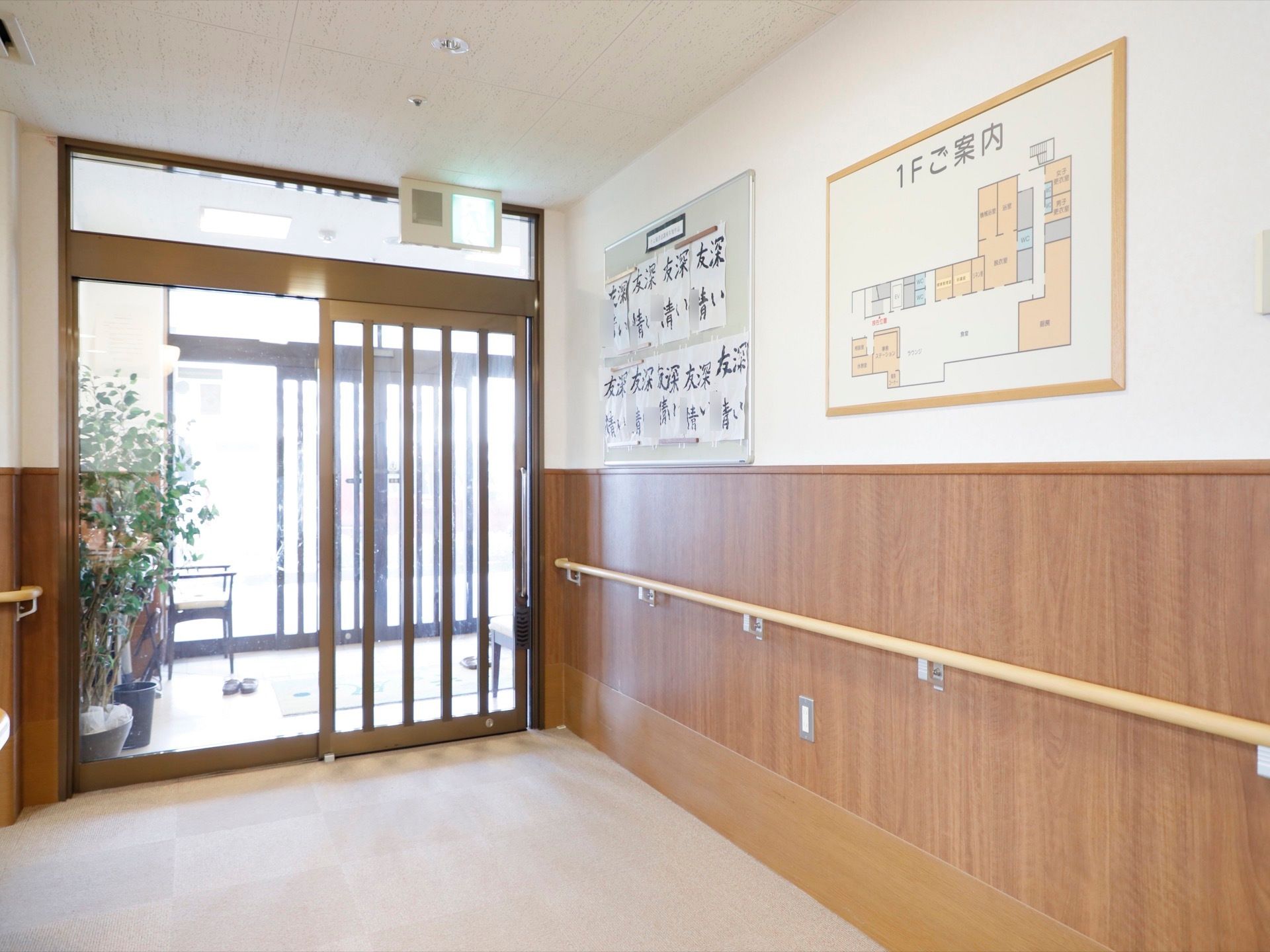 風除室があり、そこには観葉植物も置かれている。非常口の看板がある。１階の案内図が壁に掛けられている。