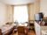 大きな窓から光の差し込む部屋に、介護用ベッドや収納棚、テレビなど生活用品が設置されている。隅には歩行器も置かれている。