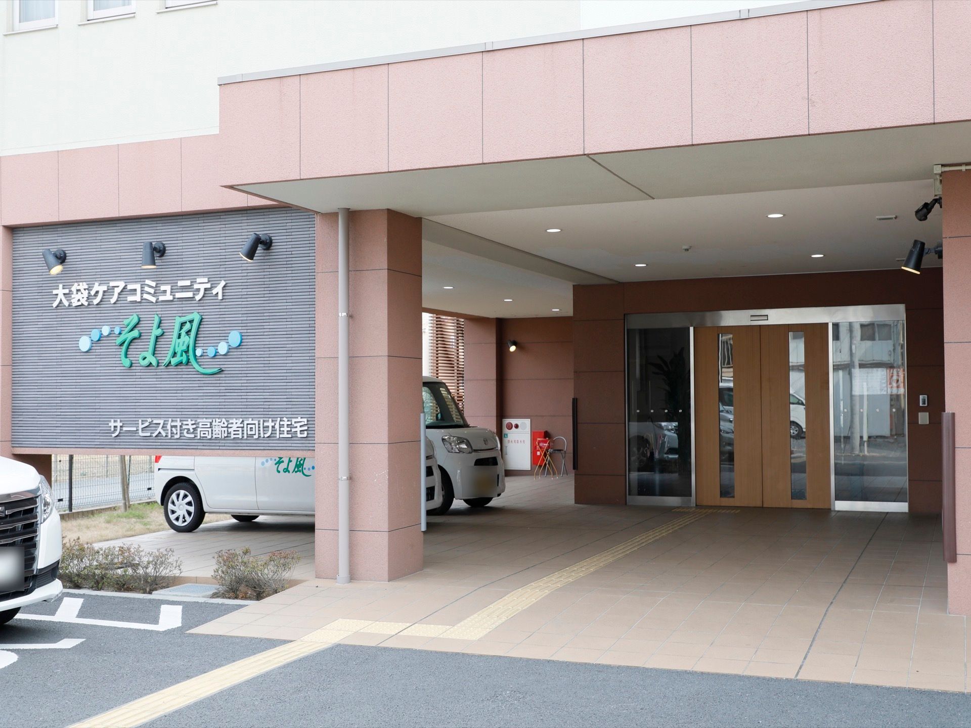 施設玄関の様子。ブラウンと木目が基調の玄関で、自動扉が設置されている。駐車場から玄関までは段差がない。