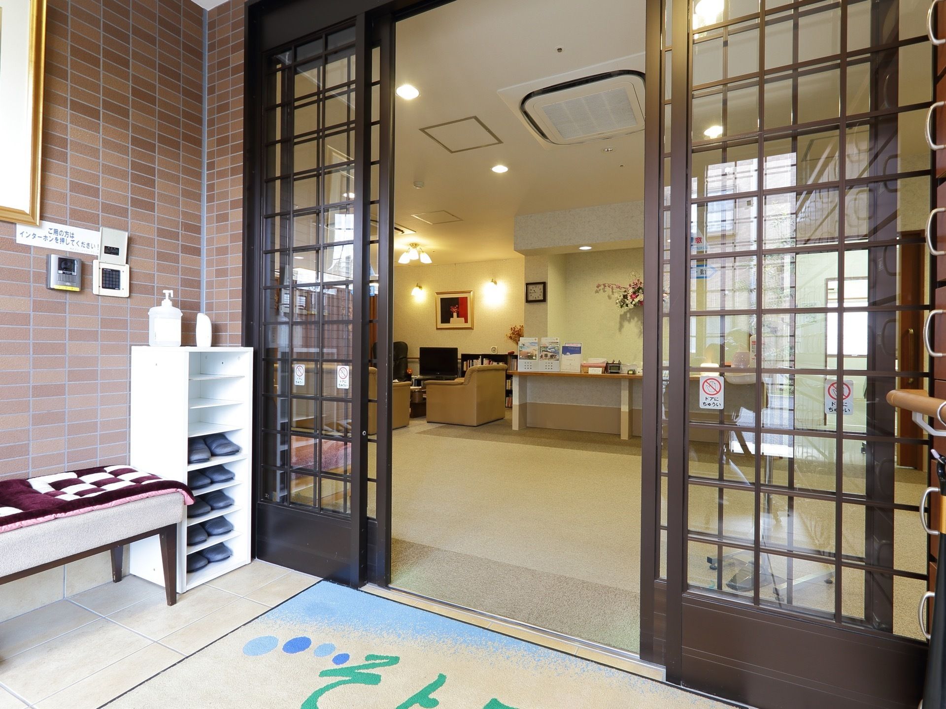 玄関は茶色い枠をした自動ドアが二重になった風除室のある構造で、入居者様用の靴箱はその中に設置されている。