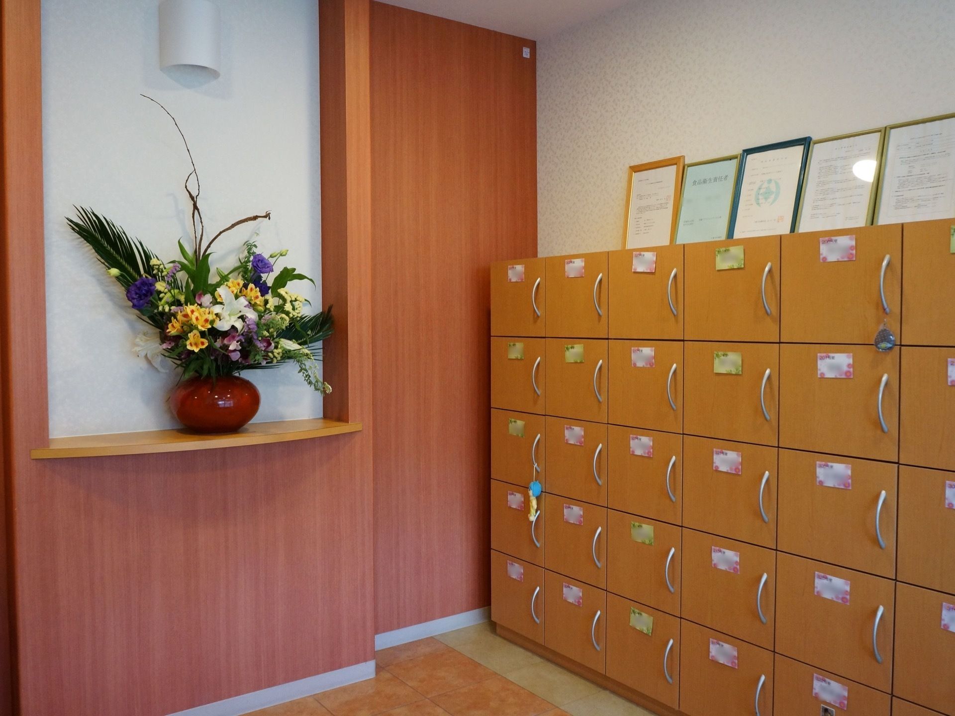 玄関正面の壁に設けられた棚には、花瓶に入った花が飾られいる。右側には、扉付きの靴箱が設置されている。