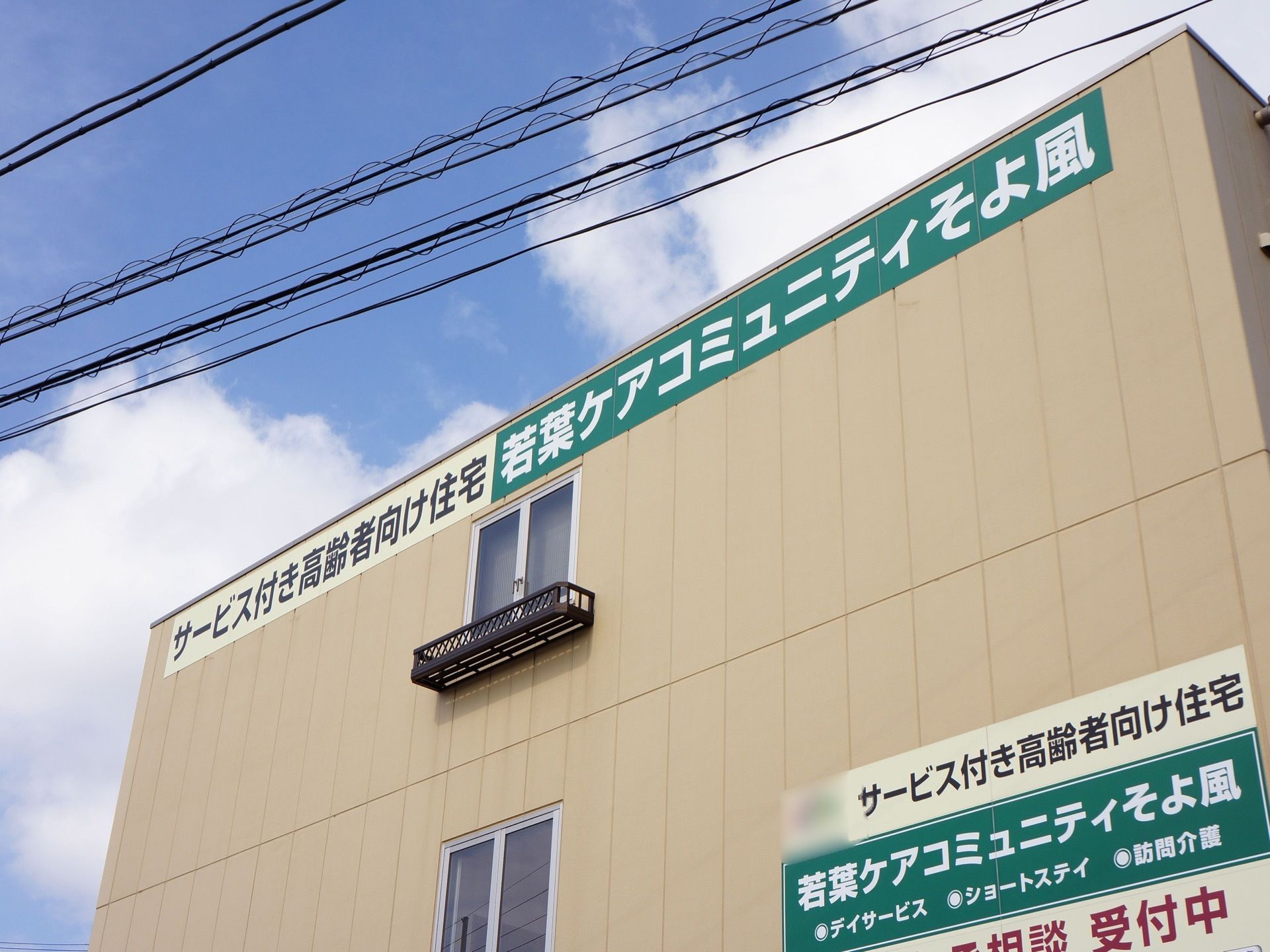 ２階と３階部分のクリーム色の３階建ての施設である。壁に窓が設けられており、外壁に大きく施設名が書かれている。