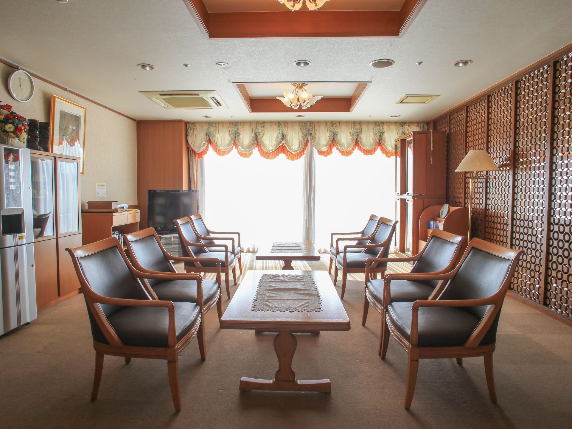 部屋の奥に大きな窓がある。座り心地の良い椅子が並べられており、その間には背の低いテーブルが用意されている。テレビや本棚が置かれている。