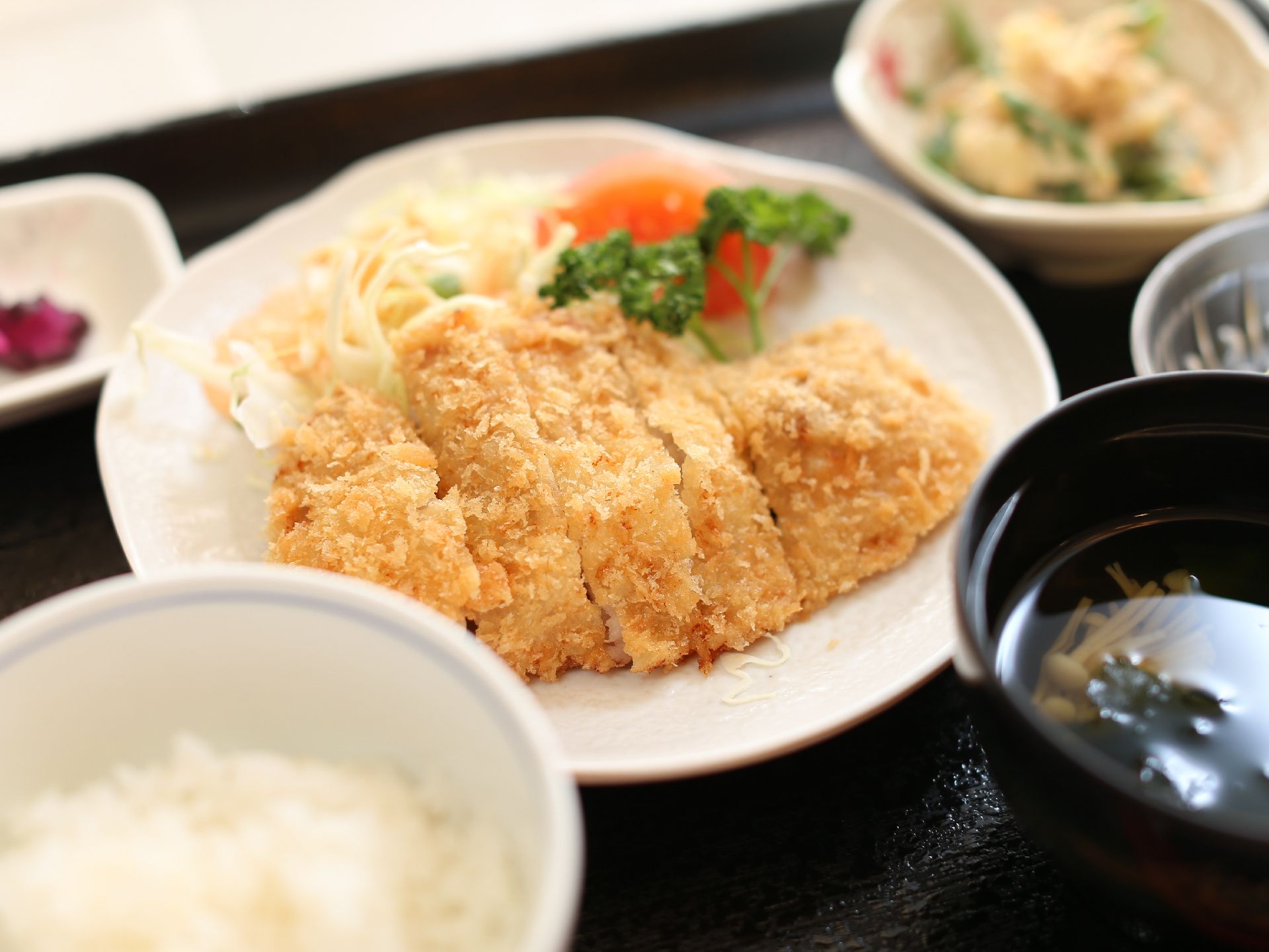 白米とお吸い物、メインのおかずや小鉢が並んでいる。とんかつは食べやすい大きさに切られており、野菜も添えられていて彩りが良い。
