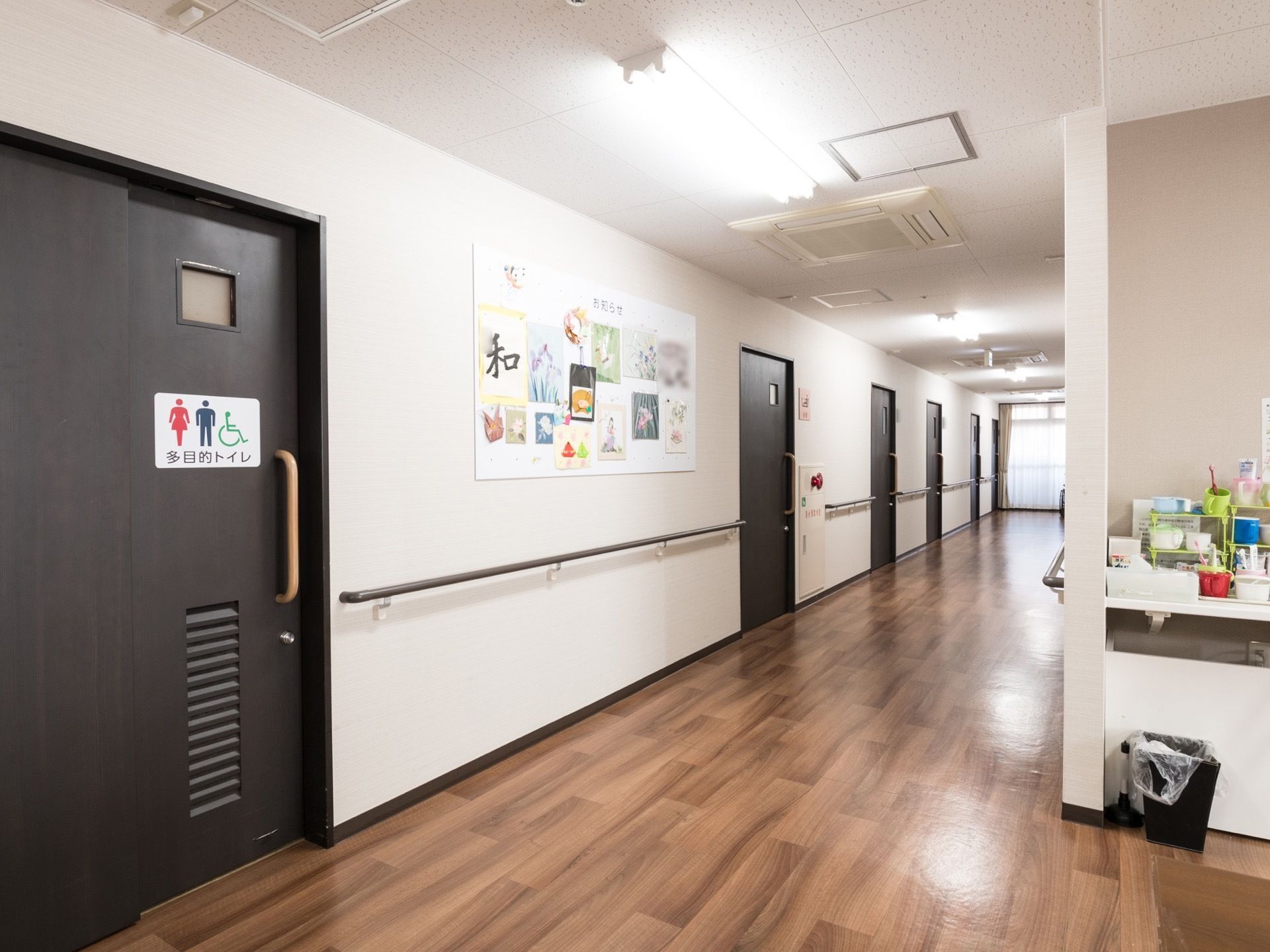 幅が広めの通路の手前には、多目的トイレがあるため、用を足すときアクセスしやすい。壁には掲示物が貼られ、居室の扉が並んでいる