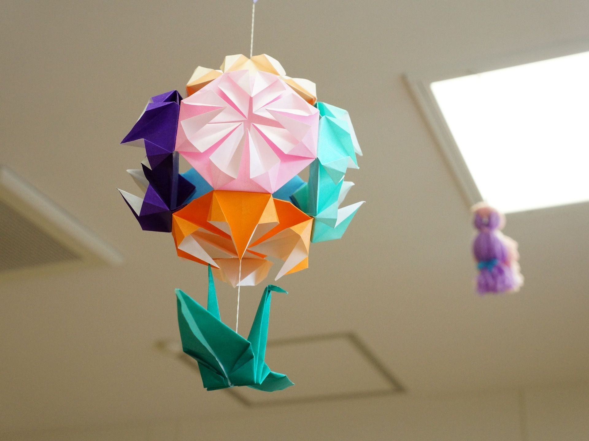 折り紙で作られた花や鶴が、紐により天井から吊り下げられている。また、奥には紫色のてるてる坊主も見える。