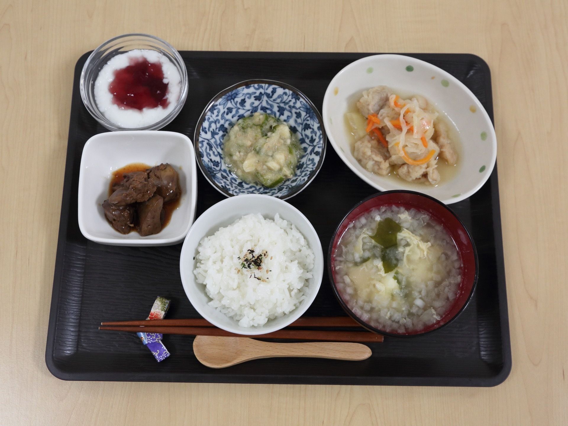 黒いトレーには、手前に箸とスプーンが添えられ、白いご飯と味噌汁、鶏肉料理と小鉢が２品、そしてデザートのヨーグルトが並んでいる。