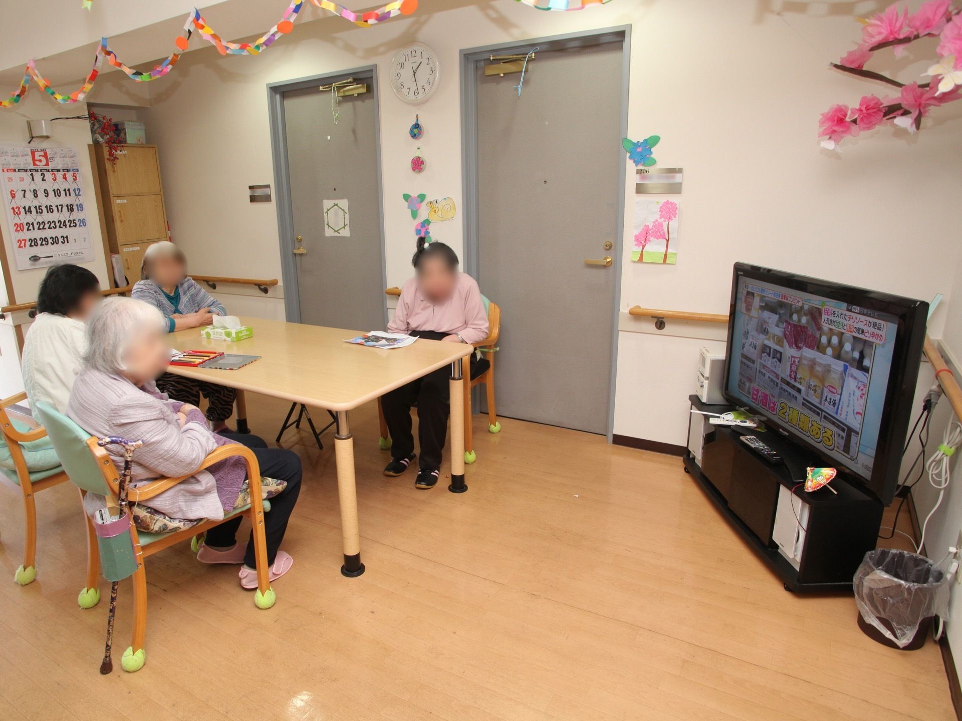 入居者様達がチェアに座って、テレビ視聴を楽しんでいる様子。壁には、スタッフお手製の装飾が施されており、楽しい雰囲気になっている。