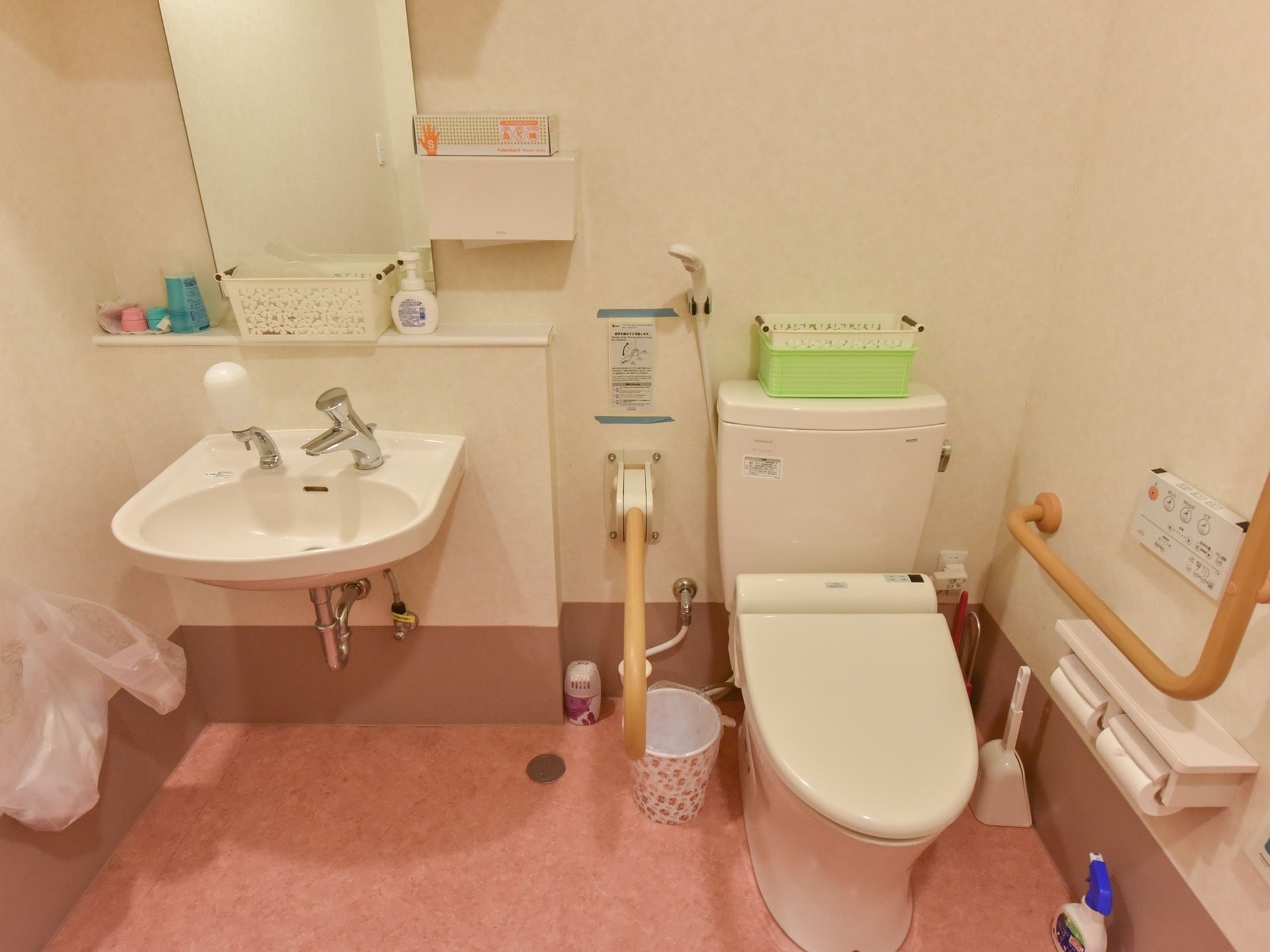 トイレの便座の両側に手すりを設置し、横側に洗面台を備えている。正面に鏡があり、その下の棚にはソープなどを置いている。