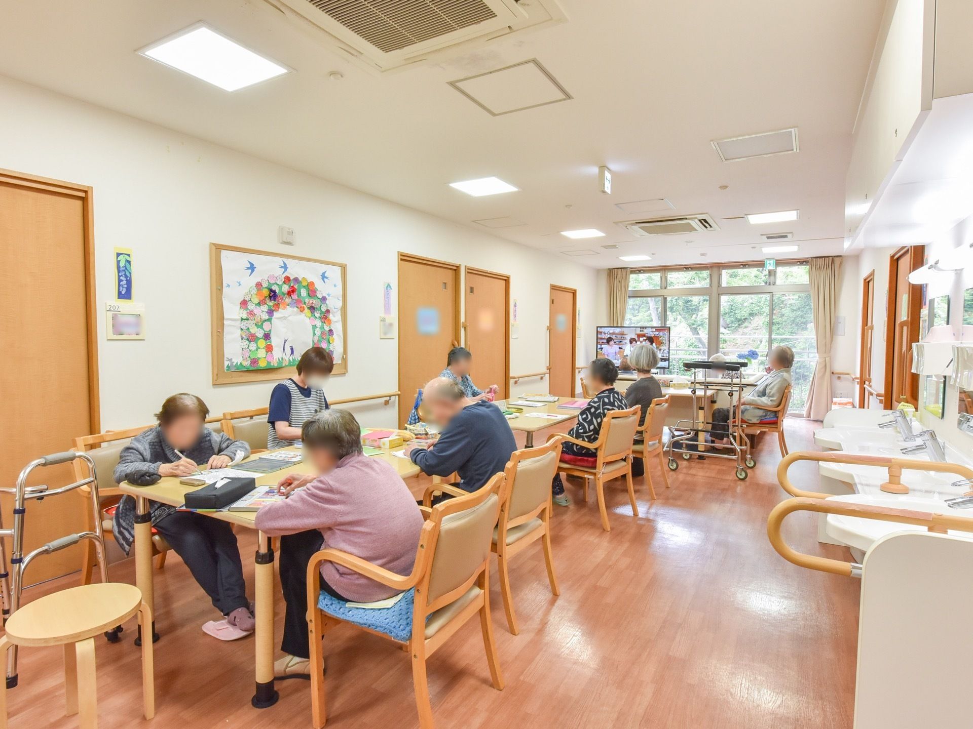 共有スペースの正面のガラス戸の外は、緑豊かな風景が広がっている。壁に手作りのレイアウトを取り入れ癒しの空間を設けている。